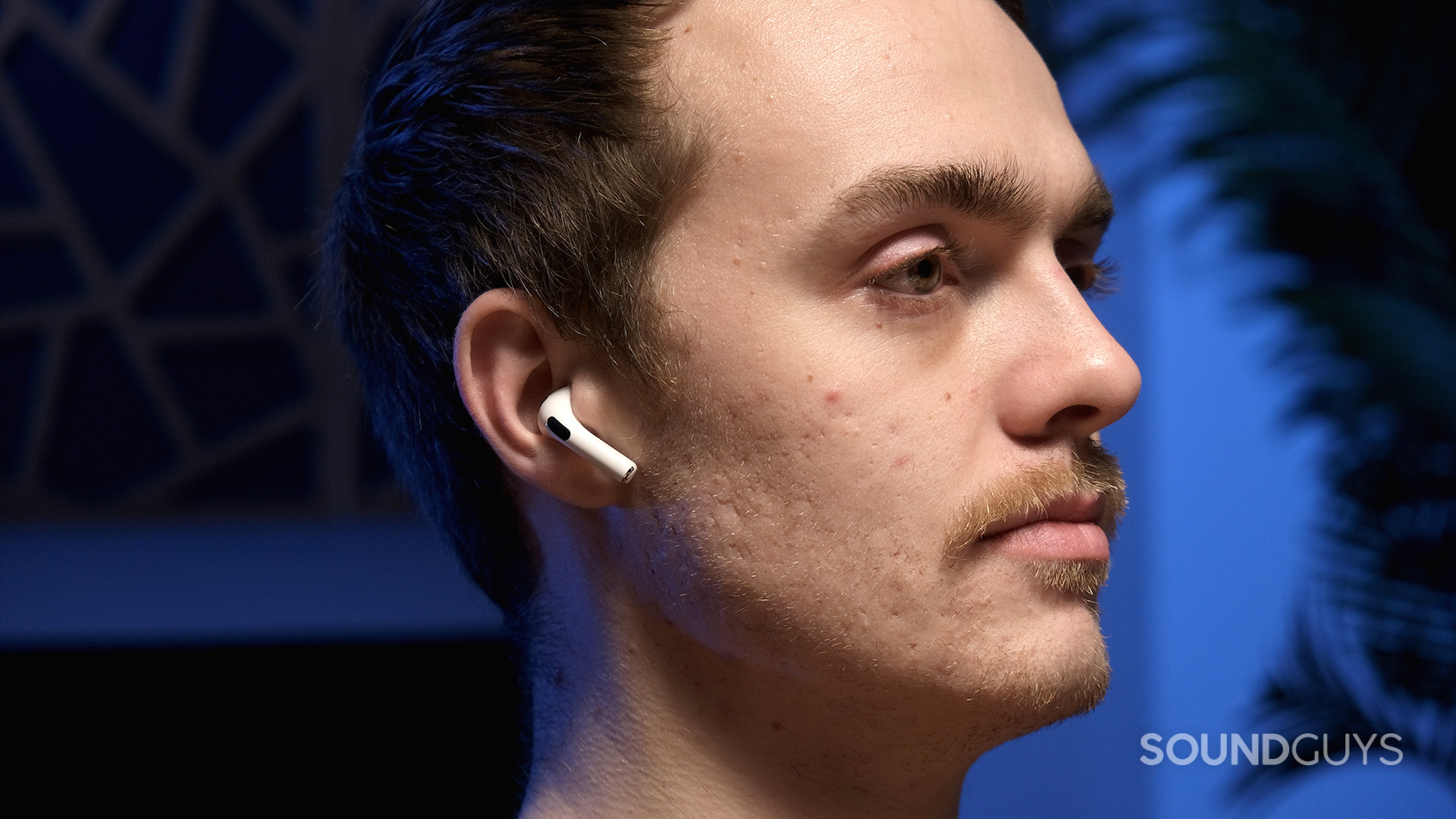 Apple AirPods 3rd Generation_1 A masculine person wears the Apple AirPods (3rd generation) against a blue background.