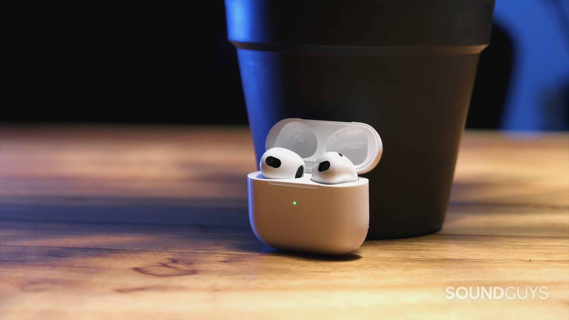 Apple AirPods 3rd Generation_4 The Apple AirPods (3rd generation) open case holds the earbuds and sits on a wood surface.