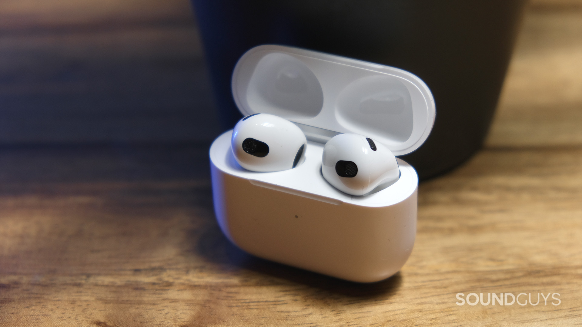 Apple AirPods 3rd Generation_5 The Apple AirPods (3rd generation) open case holds the earbuds and sits on a wood surface.