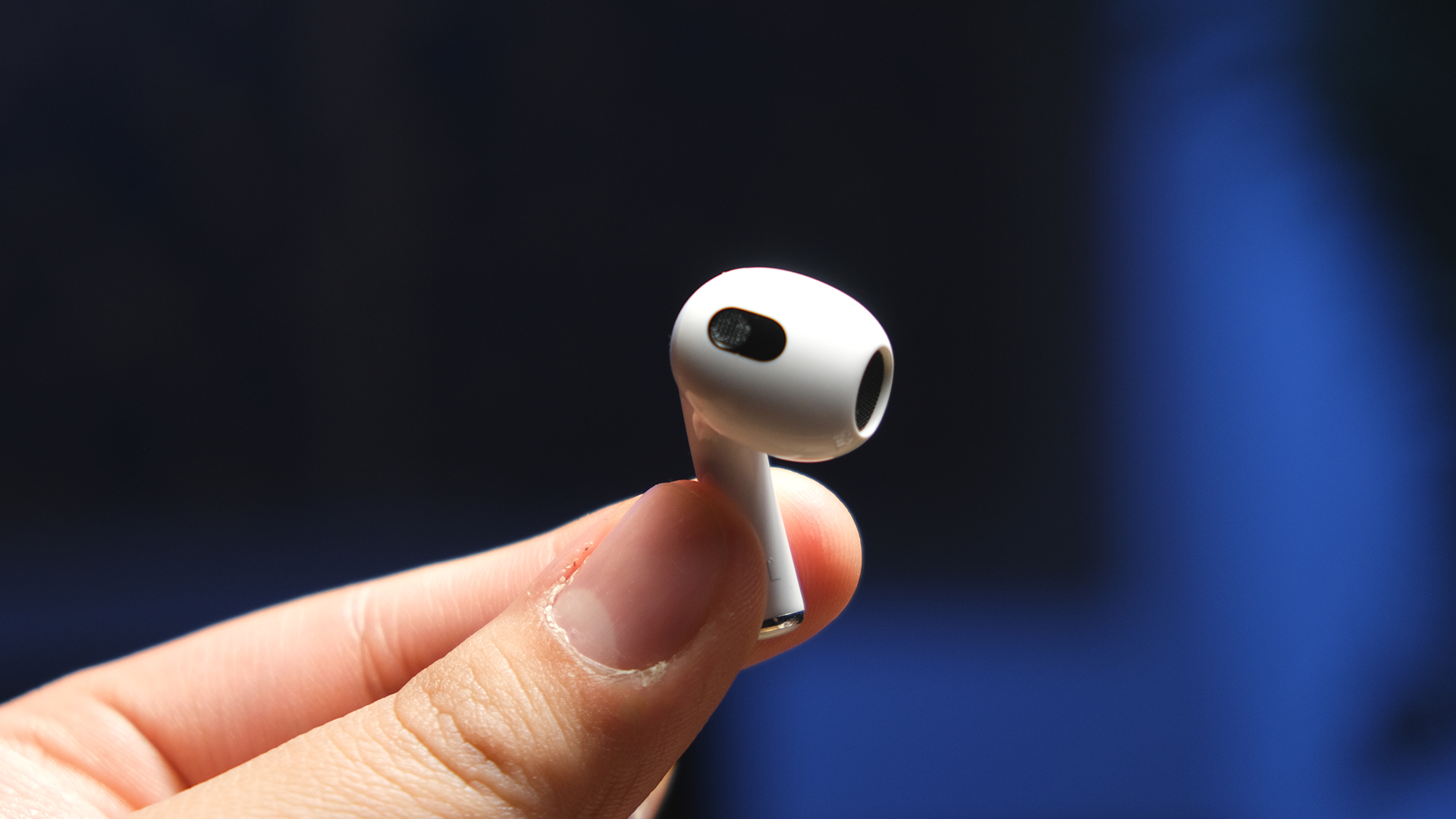 Apple AirPods 3rd Generation_9 A hand holds a Apple AirPods (3rd generation) earbud by the stem to reveal the open-type fit and embedded sensors.