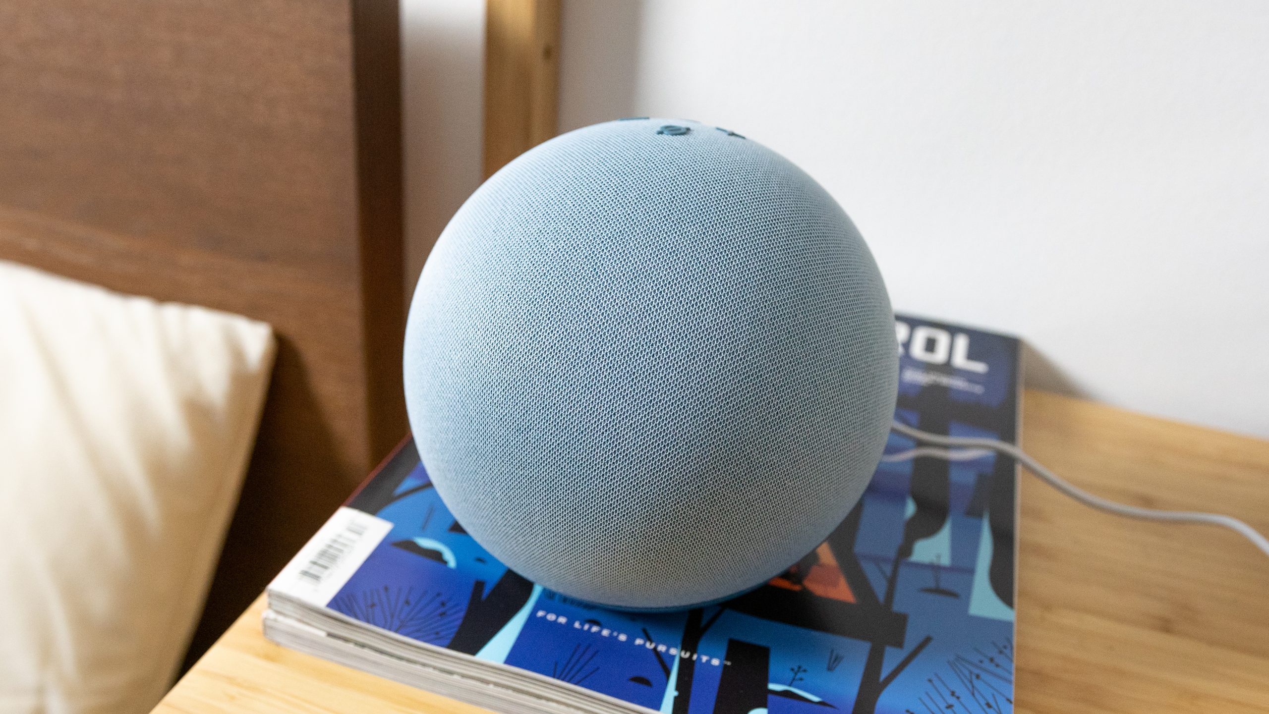 Amazon Echo 4th gen design The Amazon Echo (4th gen.) on a bedside table with bed in the background.