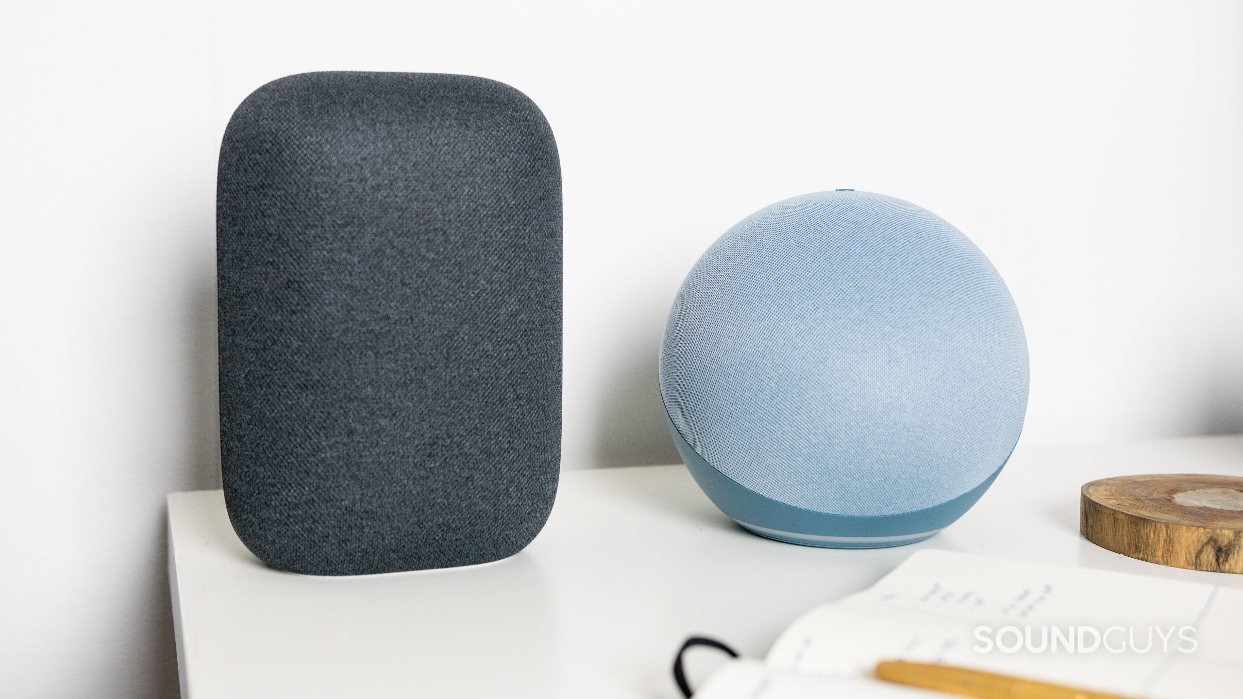 Amazon Echo 4th gen next to Google Nest Audio. Amazon Echo 4th gen next to Google Nest Audio and a notebook on a white desk.
