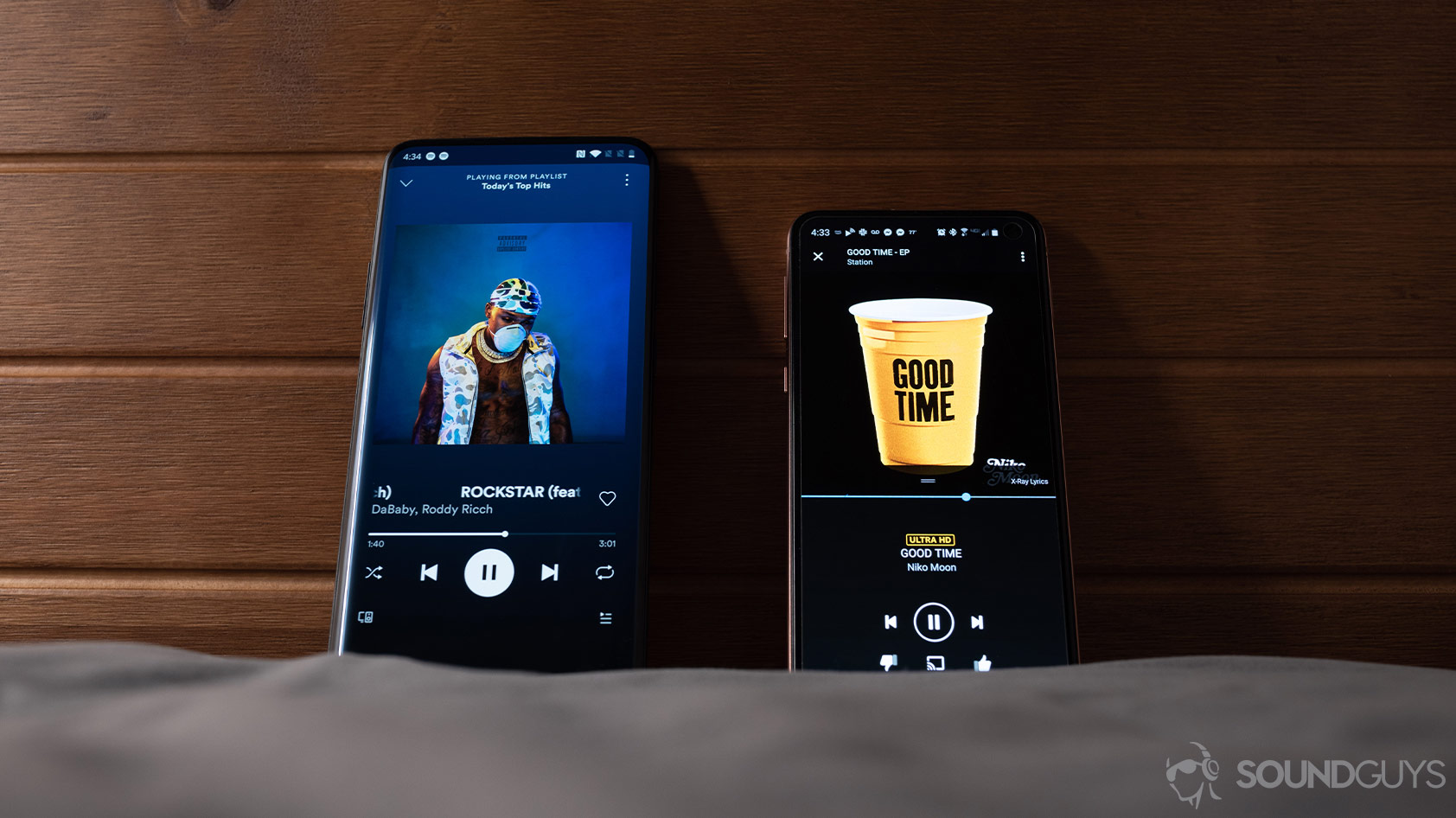 Amazon Music HD vs Spotify Premium-music streaming services comparison Amazon Music HD vs Spotify Premium music streaming services pulled up on two smartphones against a wood headboard.