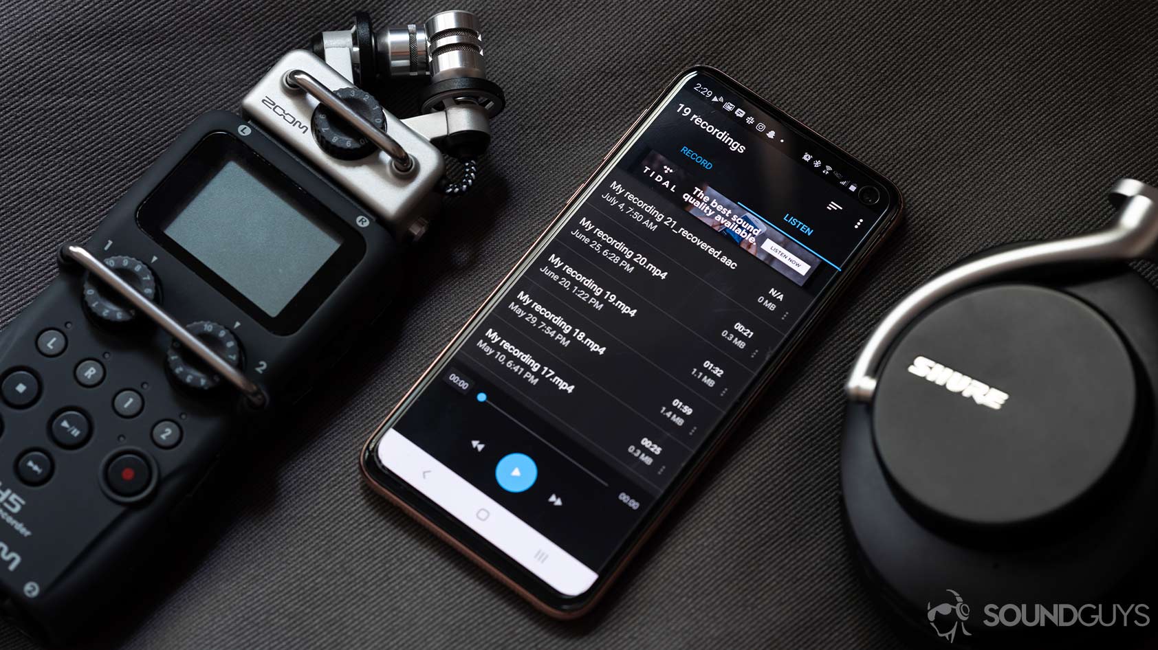 android podcast app easy voice recorder zoom recorder shure headphones A picture of the Easy Voice Recorder app on a Samsung Galaxy S10e smartphone, flanked by a Zoom recorder and Shure noise canceling headphones.