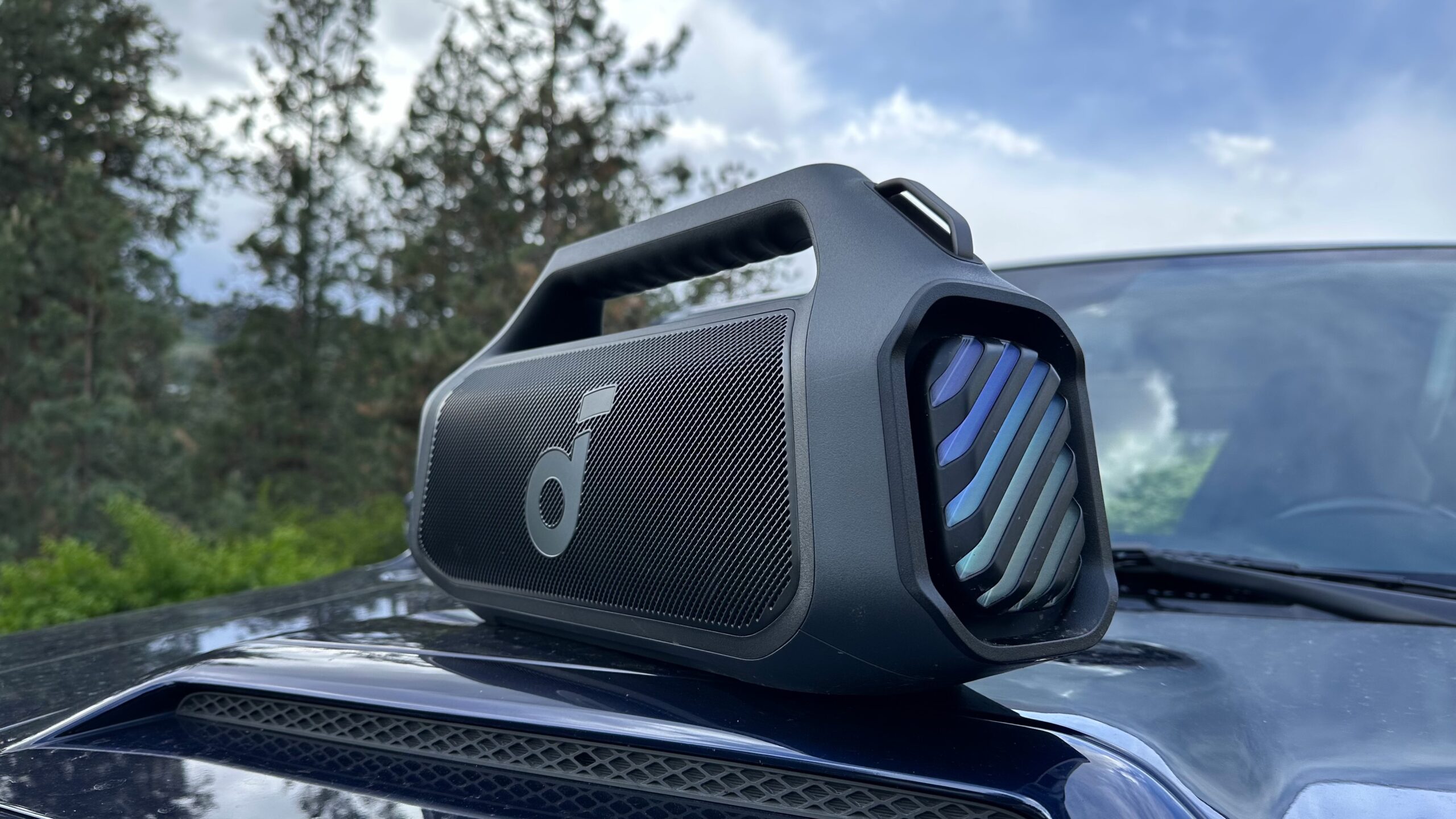 Anker Soundcore Boom 2 Plus 8 An Anker Soundcore Boom 2 Plus placed on top of an automobile hood, angled towards the camera