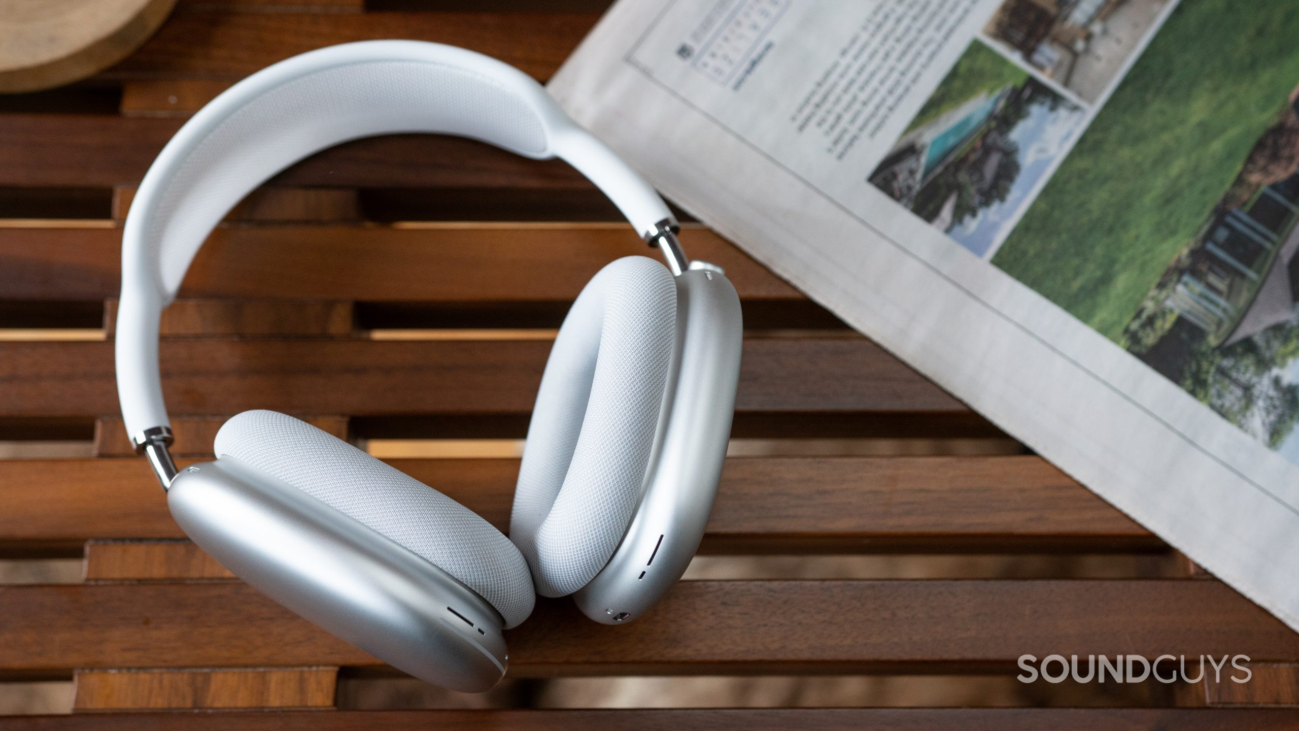 Apple AirPods Max on coffee table The Apple AirPods Max in white on a coffee table next to a newspaper.
