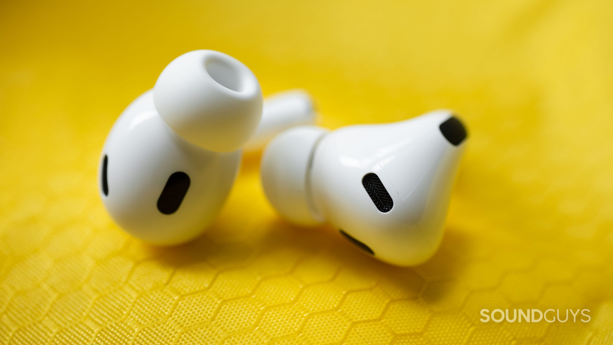 Apple AirPods Pro (2nd generation) true wireless earbuds sensors vents The Apple AirPods Pro (2nd generation) sensors decorate the earbuds which lay on a yellow, textured surface.