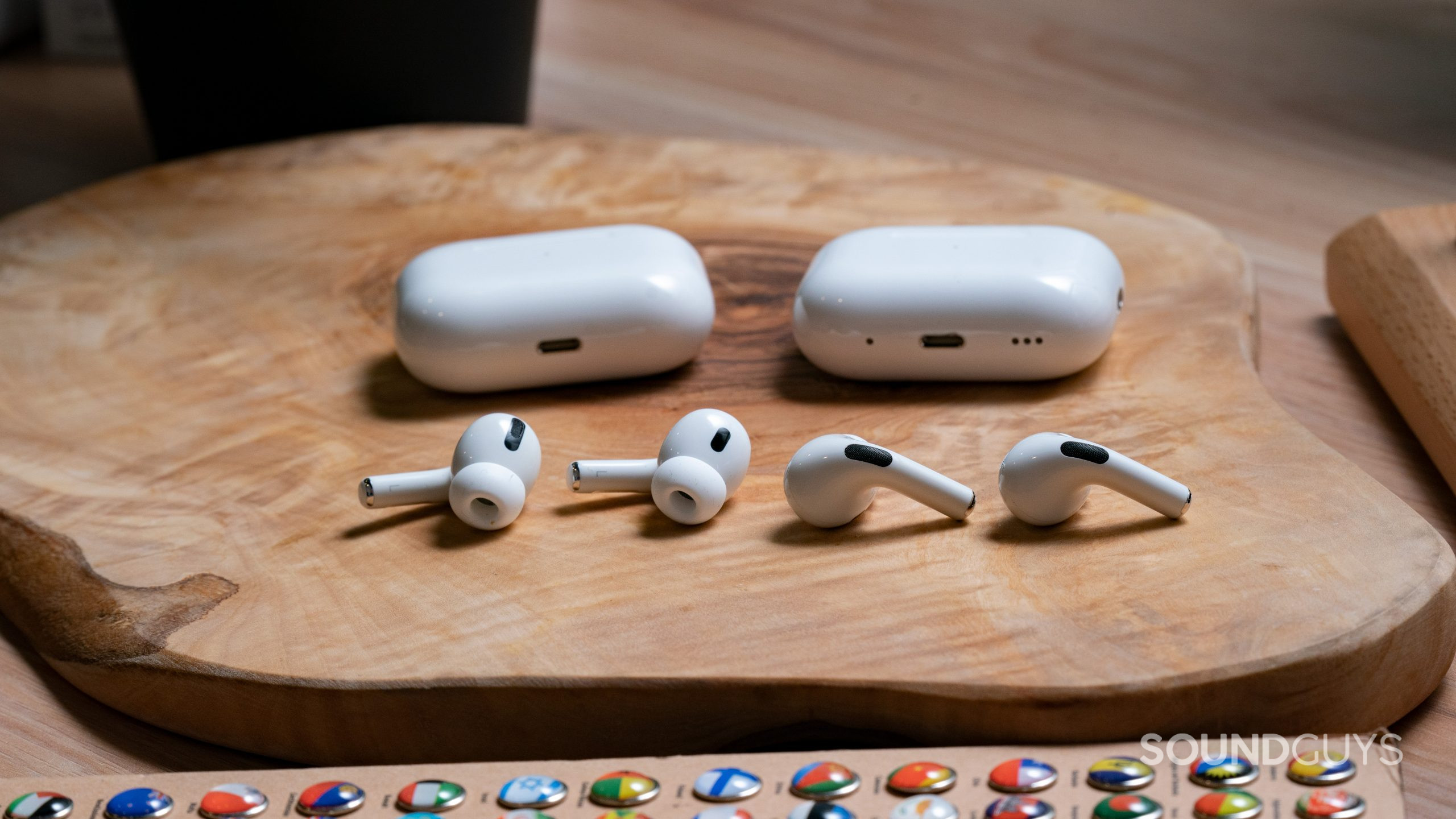 Apple Airpods Pro Gen 2 vs. Apple Airpods Pro Gen 1 Buds Comparison. The Apple AirPods Pro (2nd generation) lays on a wooden surface next to the Apple AirPods Pro (1st generation), earbuds out of case.