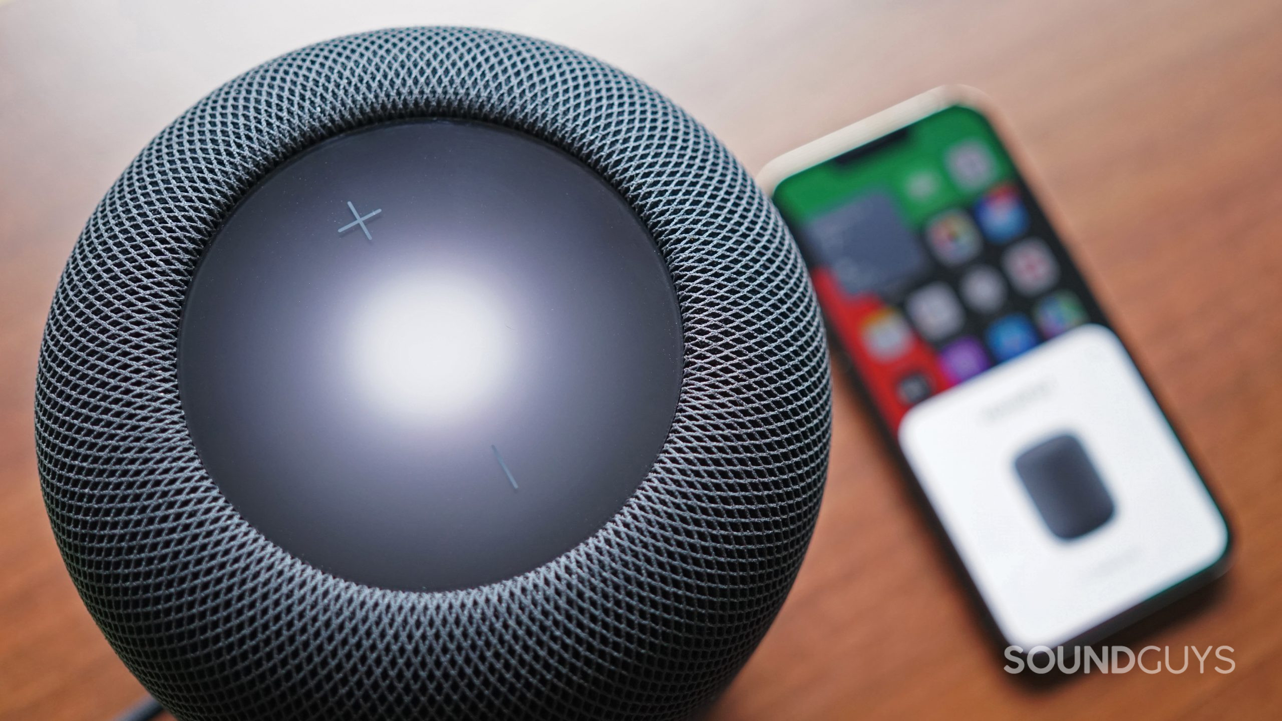 Apple-HomePod-(2nd-Generation)-iPhone-from-above An aerial close up of the Apple HomePod (2nd Generation) with the Apple iPhone 13 Pro in the background.
