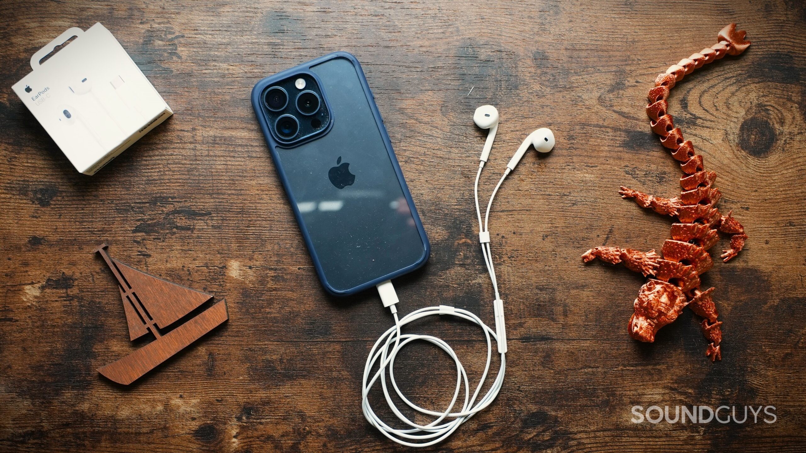 AppleEarPodsUSB-C Apple EarPods (USB-C) plugged into a blue iPhone on a wooden table next to a copper 3D printed Dragon and a wooden cutout of a boat.