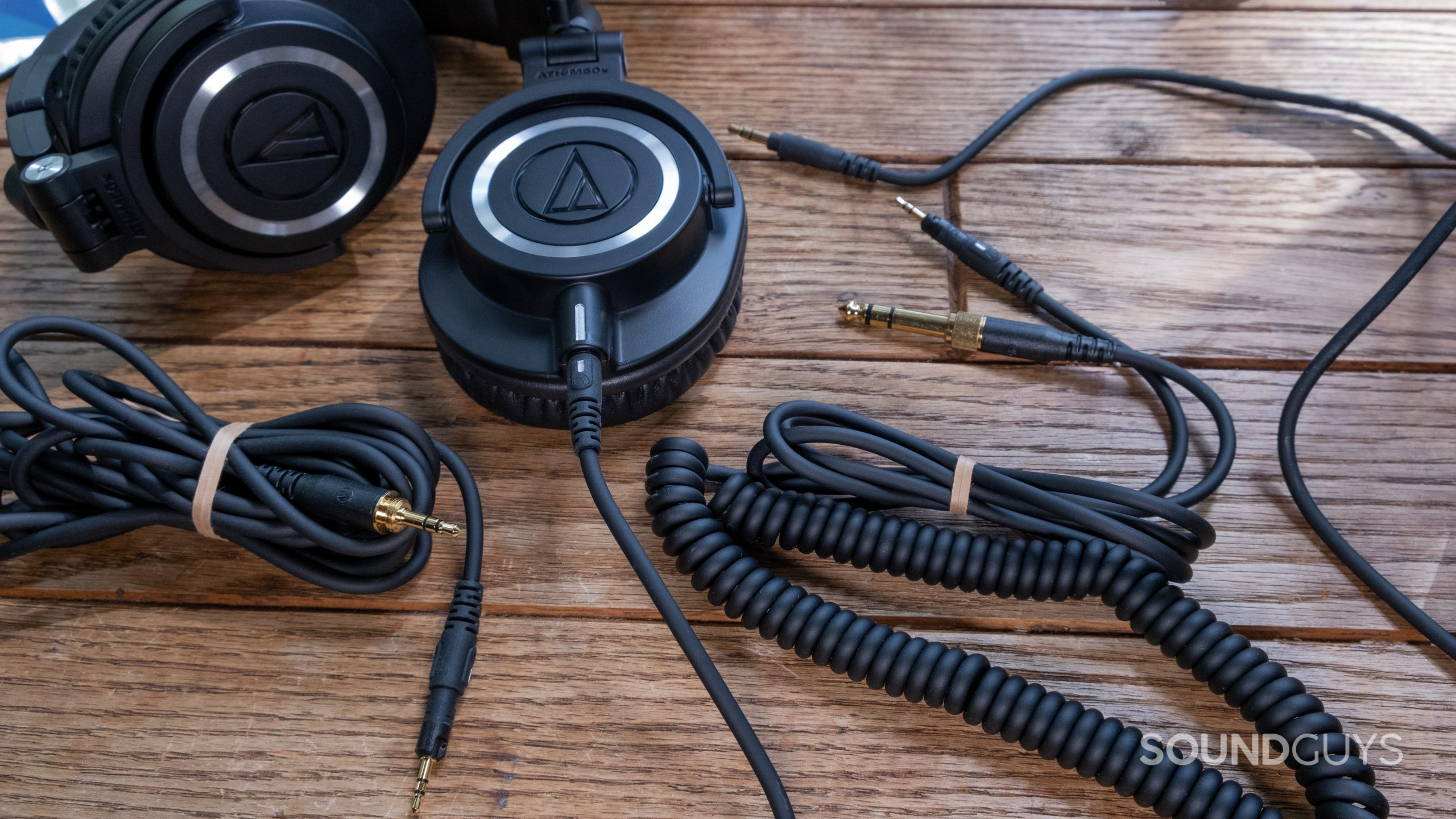 audio-technica-ath-m50x-cables The Audio-Technica ATH-M50x lays partially folded on a wood surface surrounded by all three included cables.