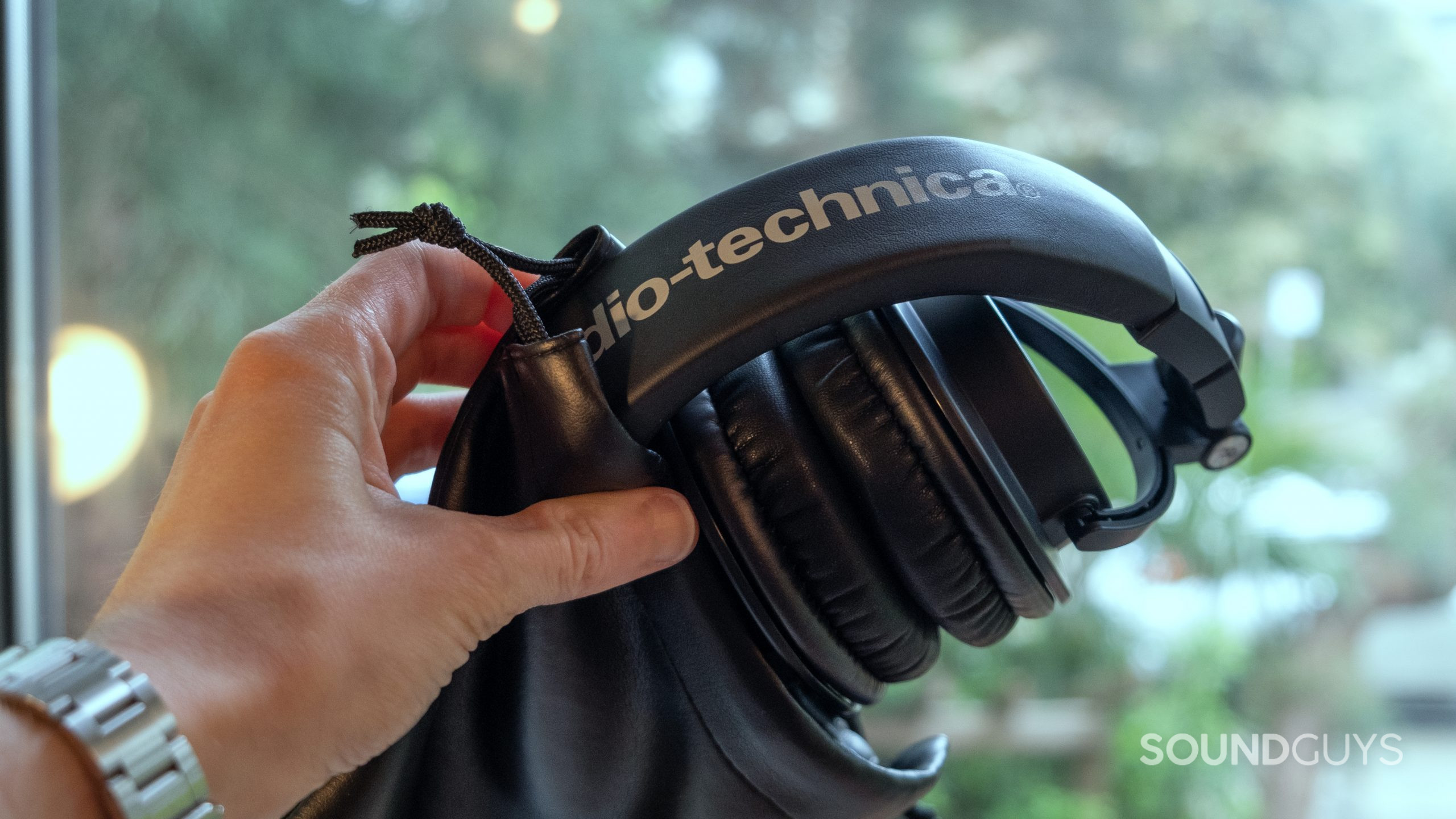 audio-technica-ath-m50x-folded-in-bag A hand holds the folded up Audio-Technica ATH-M50x partially inside its vinyl carry bag.