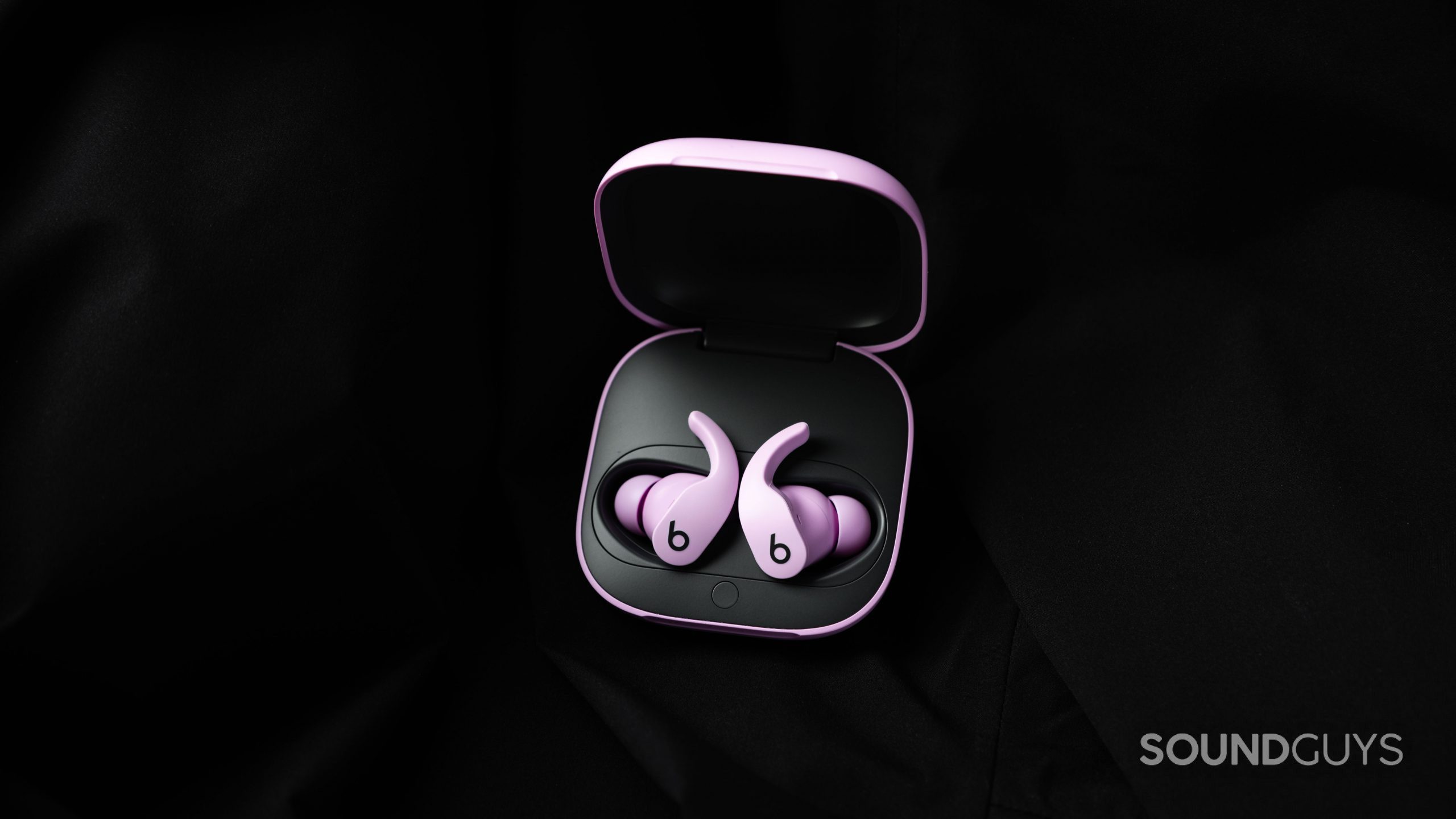 Beats Fit Pro noise canceling true wireless earbuds open case The Beats Fit Pro noise canceling true wireless earbuds in purple lay in the open charging case against a black fabric background.