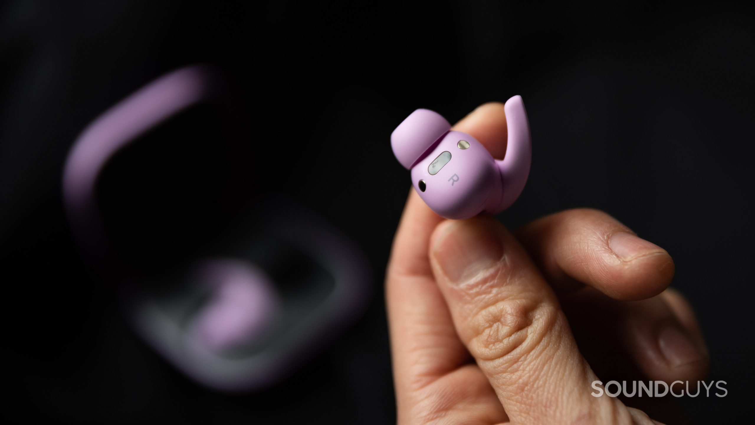 Beats Fit Pro noise canceling true wireless earbuds sensor hand A hand holds the Beats Fit Pro noise canceling true wireless earbud in purple to display its sensors, magnets, and wing tip extension.