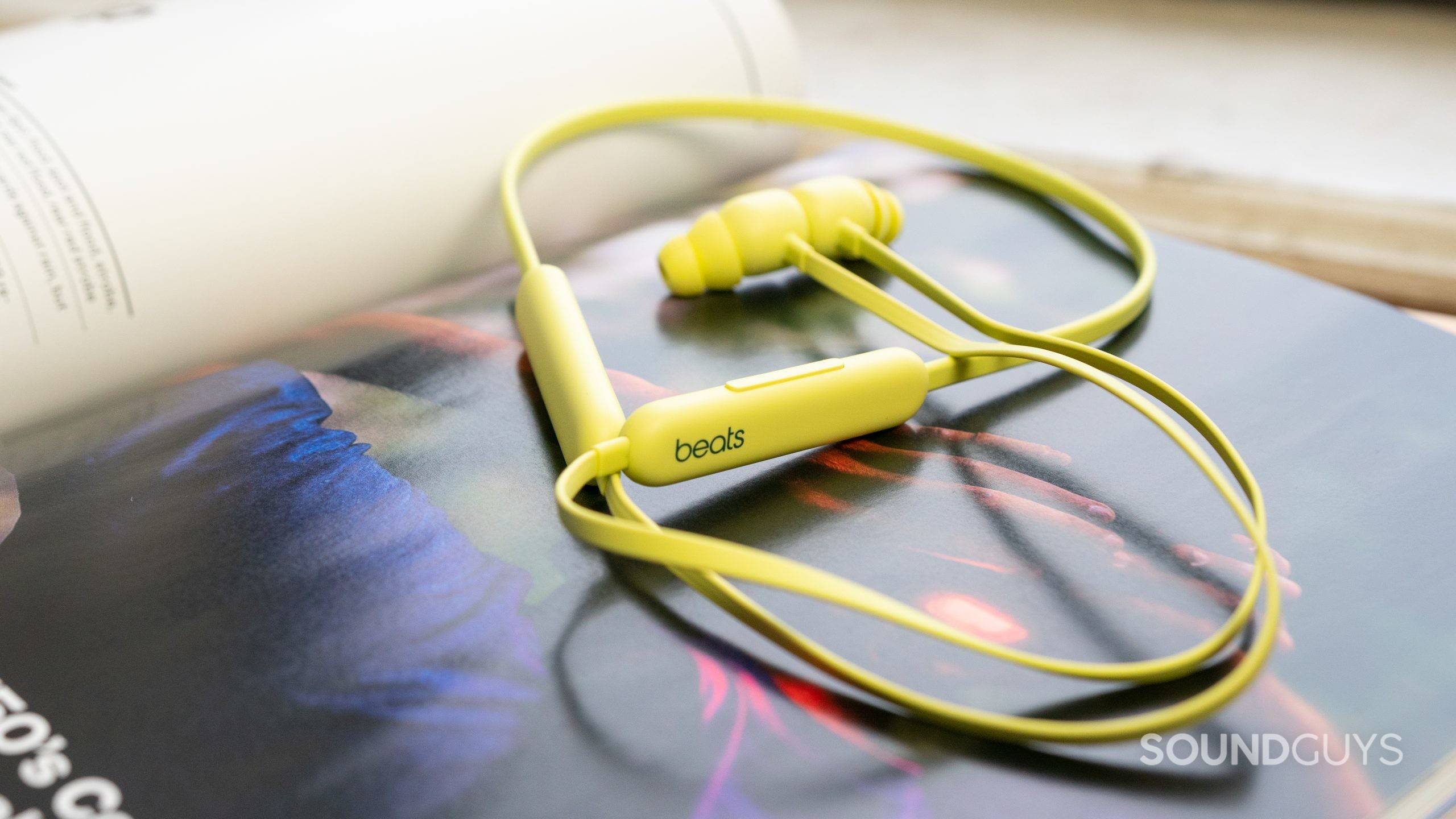 Beats Flex anti-tangle. Beats Flex earbuds in yellow on an open magazine by the window.