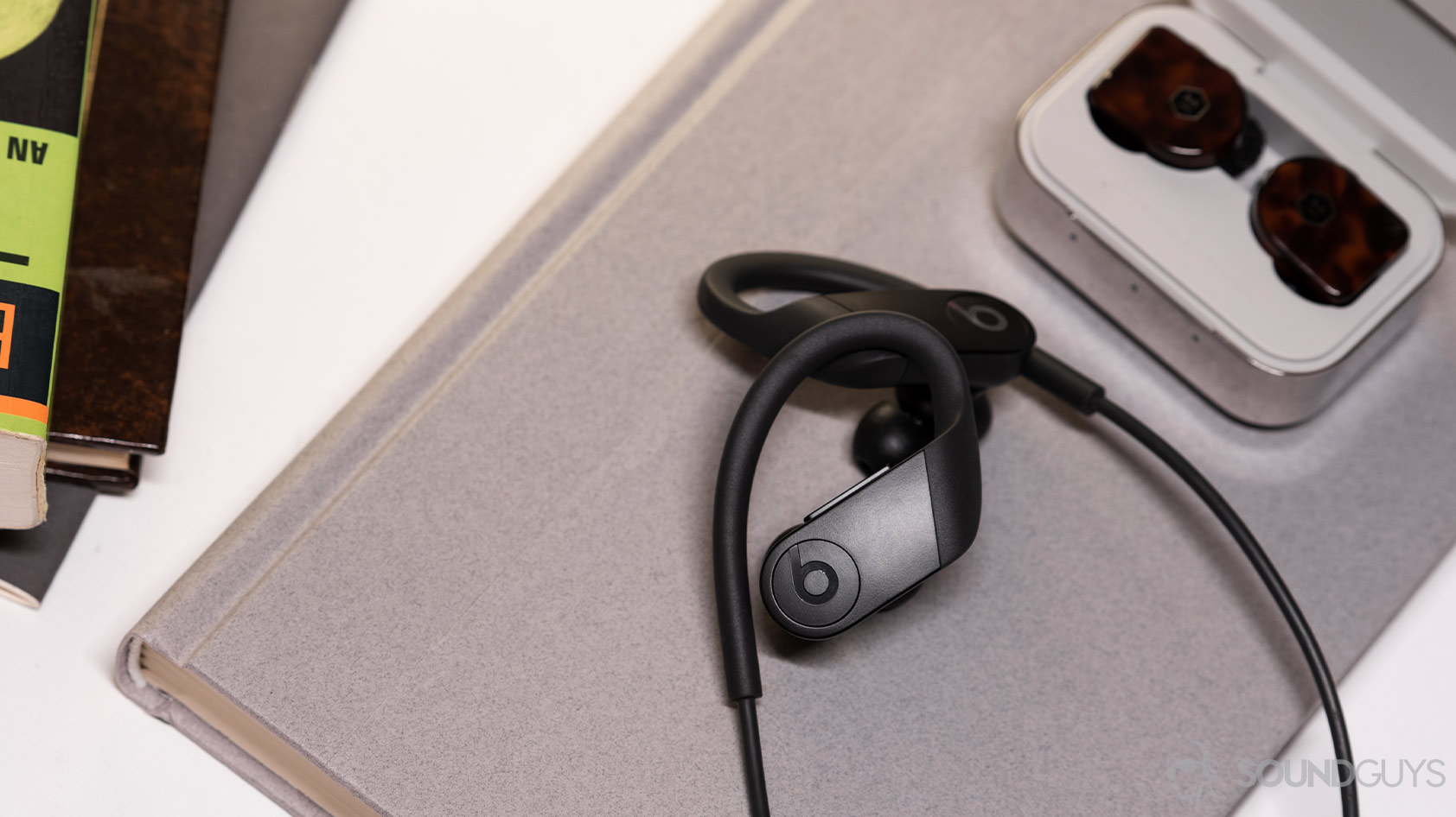 Beats Powerbeats-wireless workout earbuds master dynamic mw07 plus noise canceling earbuds A picture of the Apple Beats Powerbeats on a book and next to the Master & Dynamic MW07 Plus true wireless noise cancellinlg earphones.