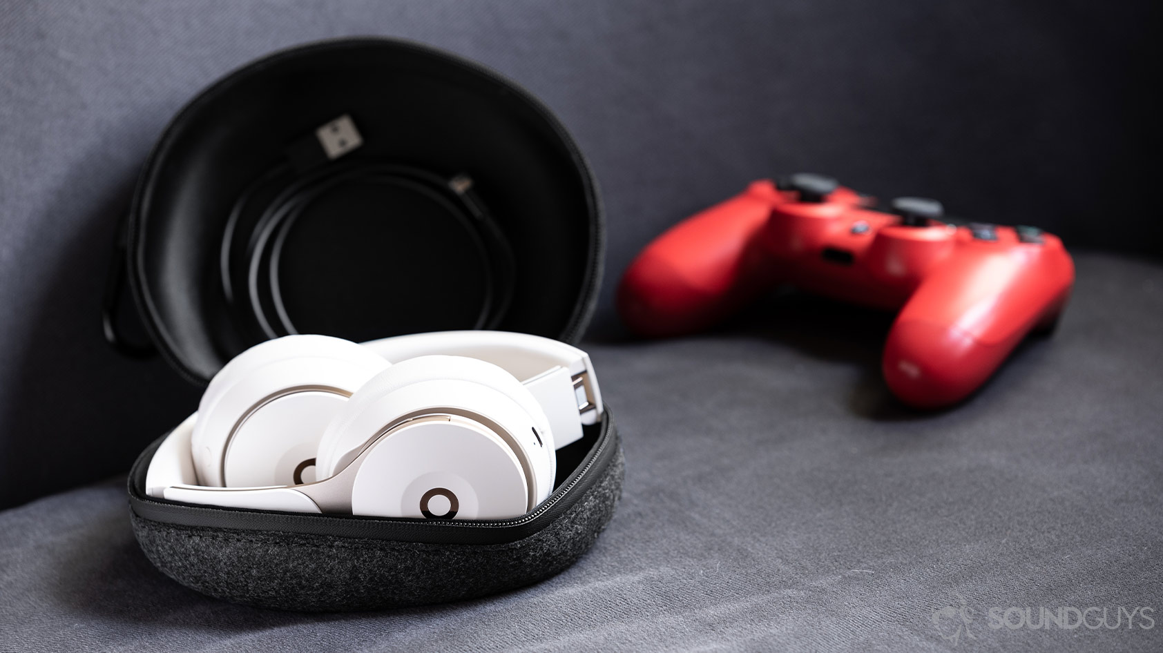 Beats Solo Pro-noise canceling headphones folded carrying pouch PlayStation 4 controller A photo of the Beats Solo Pro on-ear noise canceling headphones folded in the cloth carrying pouch with the included Lightning cable and a PS4 controller (red) in the background.