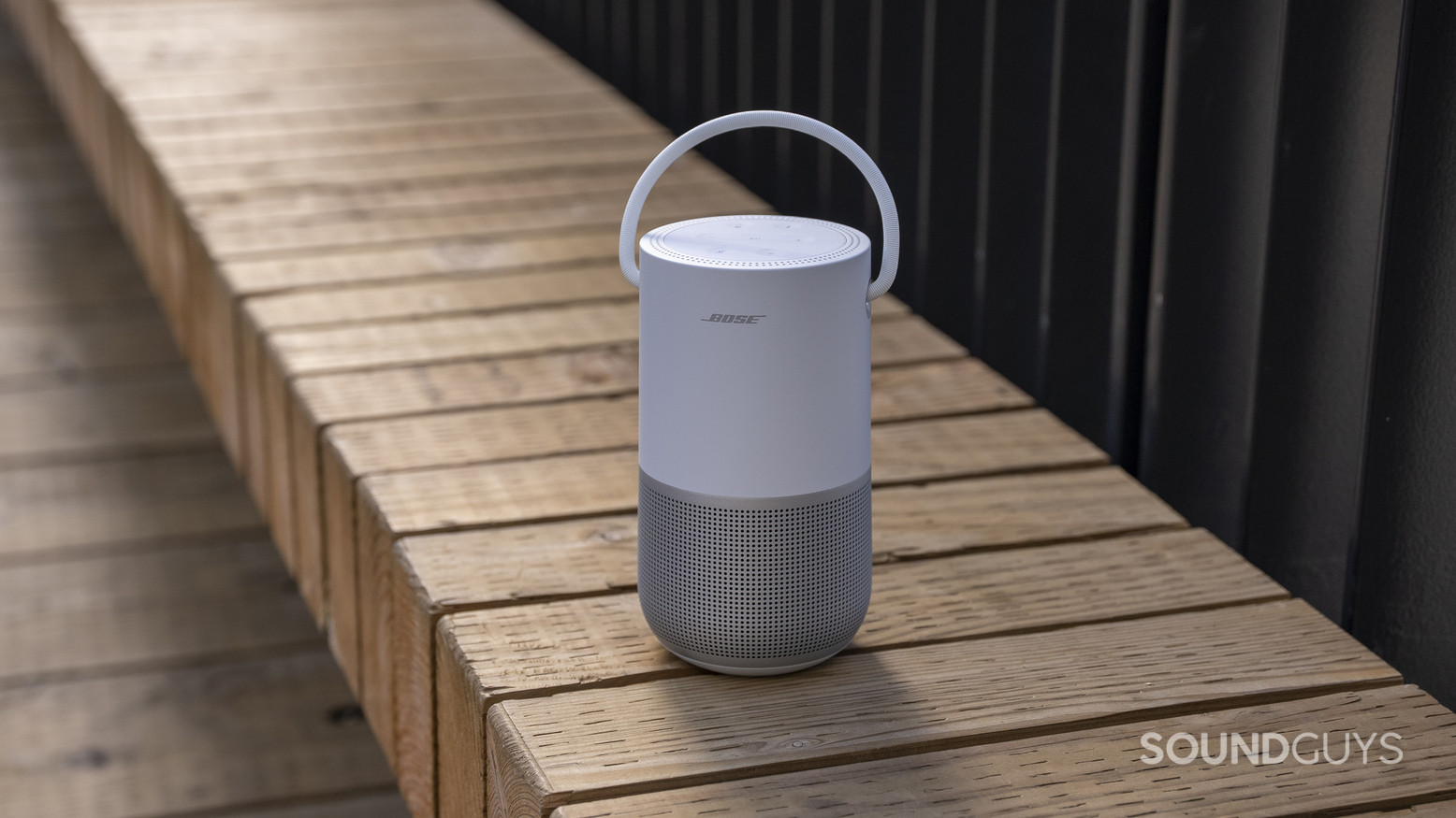 bose-portable-smart-speaker-8 A Bose Portable Smart Speaker sitting on a wooden bench outdoors.