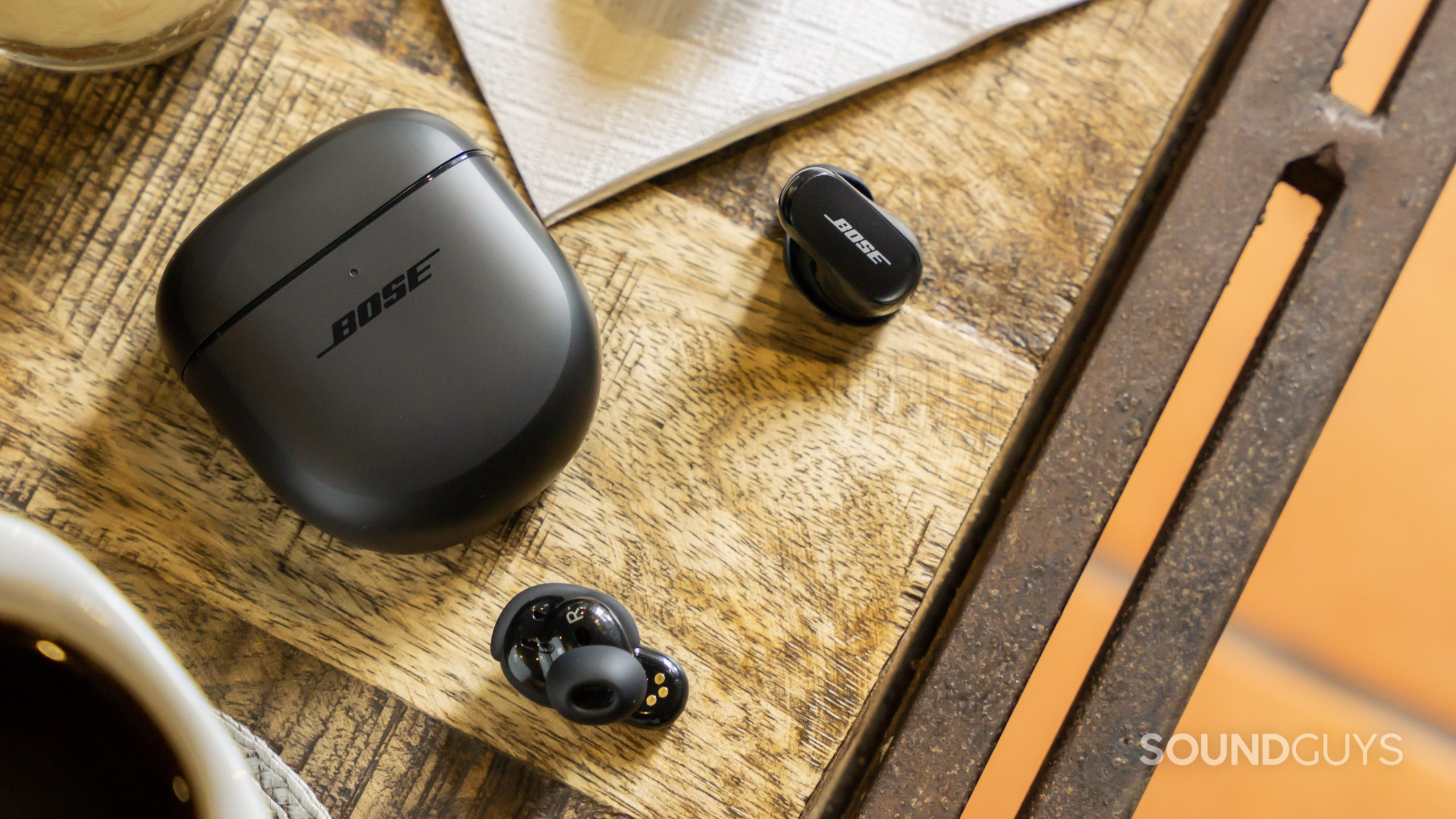 bose-quietcomfort-earbuds-ii-table-case The Bose QuietComfort Earbuds II lays on a wooden table with coffee in the corner.