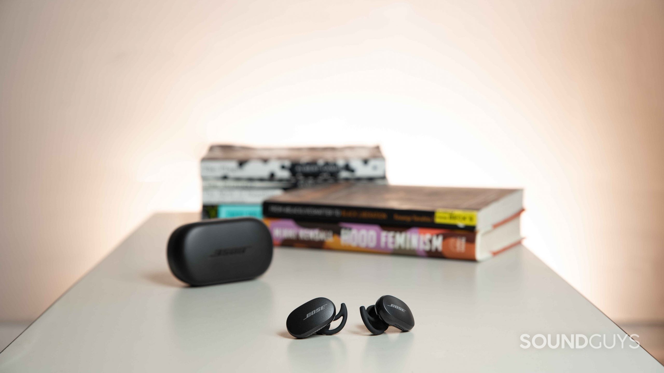 Bose QuietComfort Earbuds noise canceling true wireless-5 The Bose QuietComfort Earbuds noise canceling true wireless earbuds rest outside of the charging case on a table and in front of a stack of books.