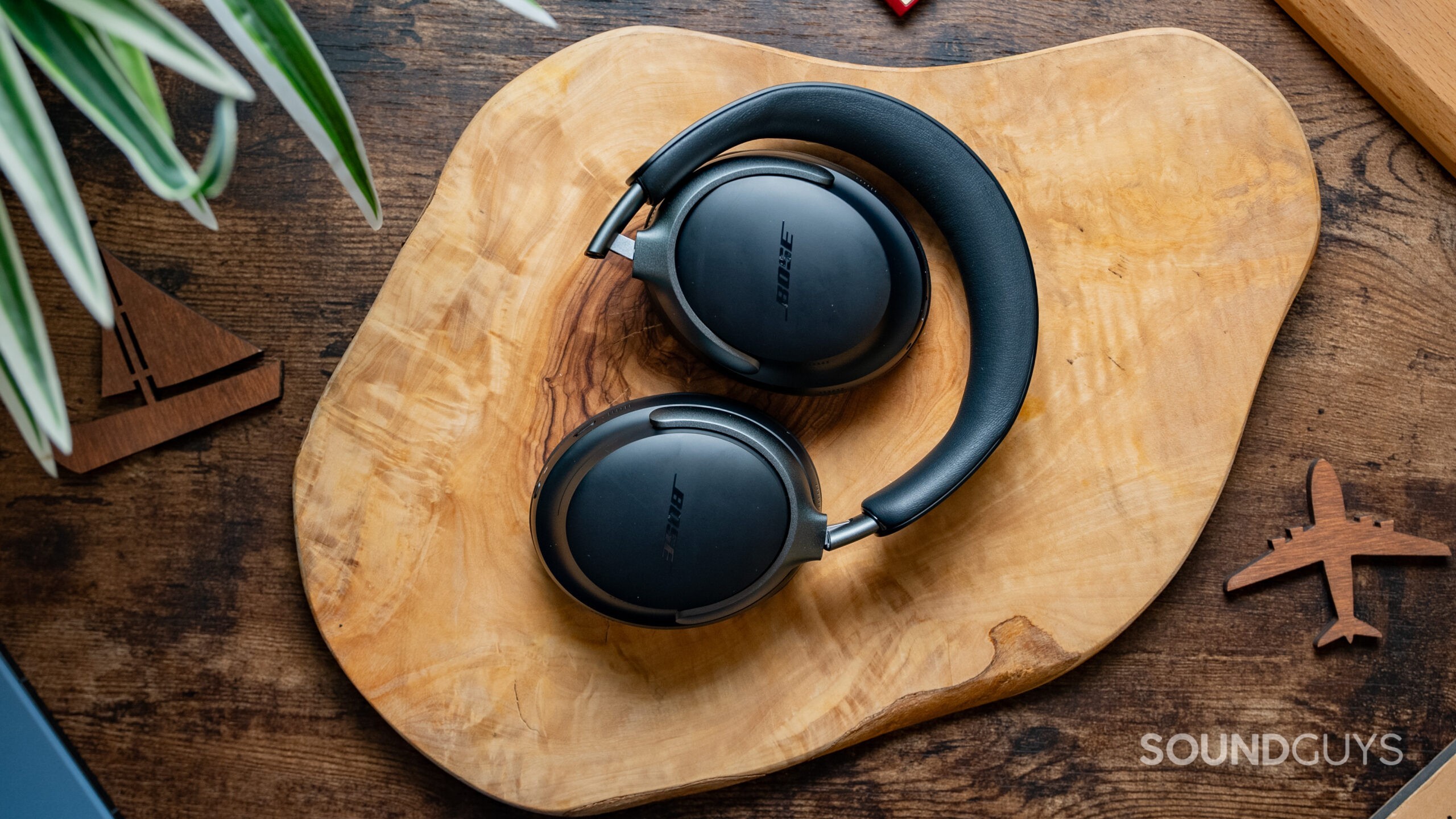 Bose Quietcomfort Ultra Headhones Featured Image #1 The Bose QuietComfort Ultra Headphones lying atop a wood slab.