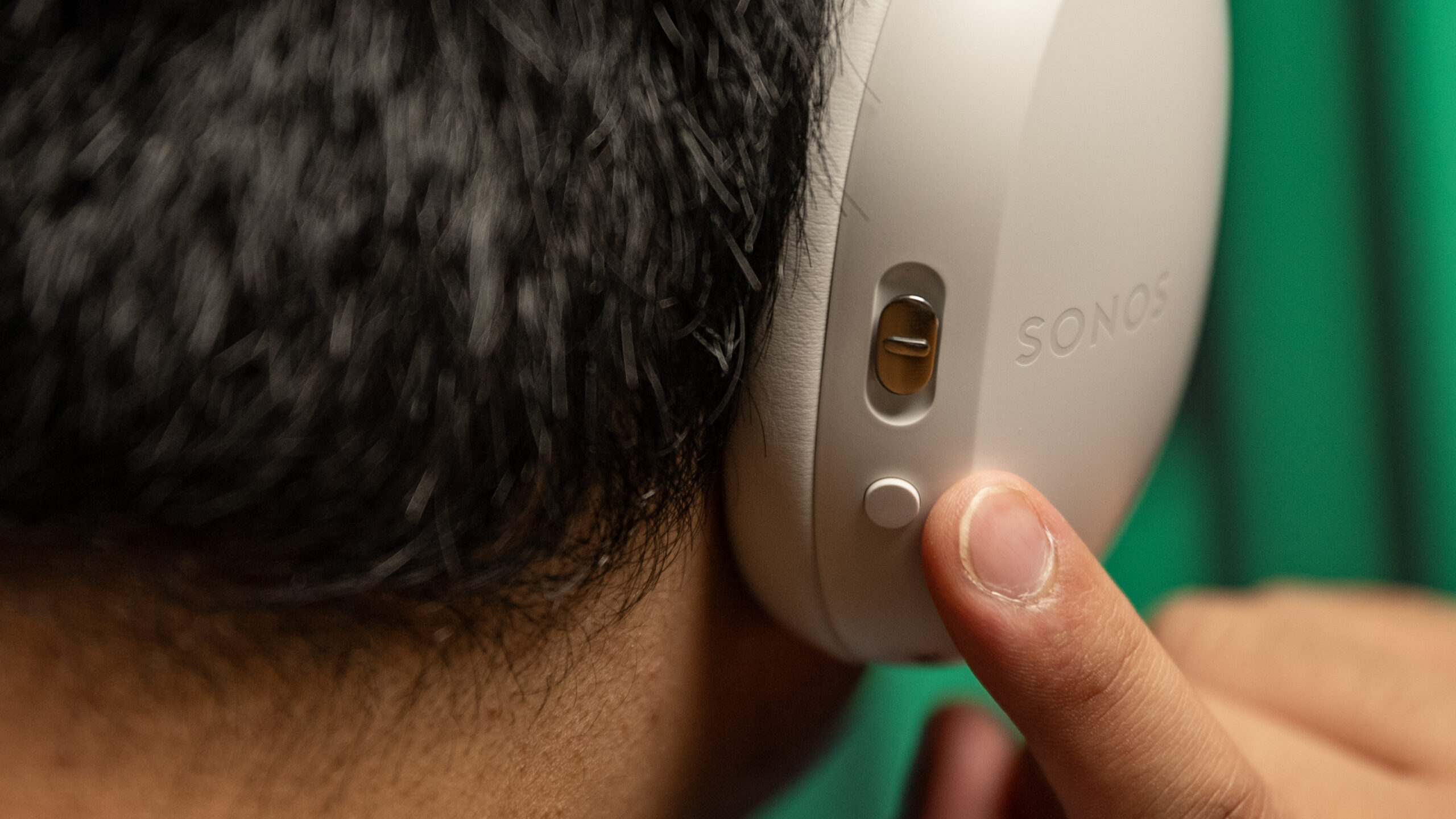 Sonos Ace wearing touching controls Photo of a man wearing the Sonos Ace headphones touching the noise control button and content key slider