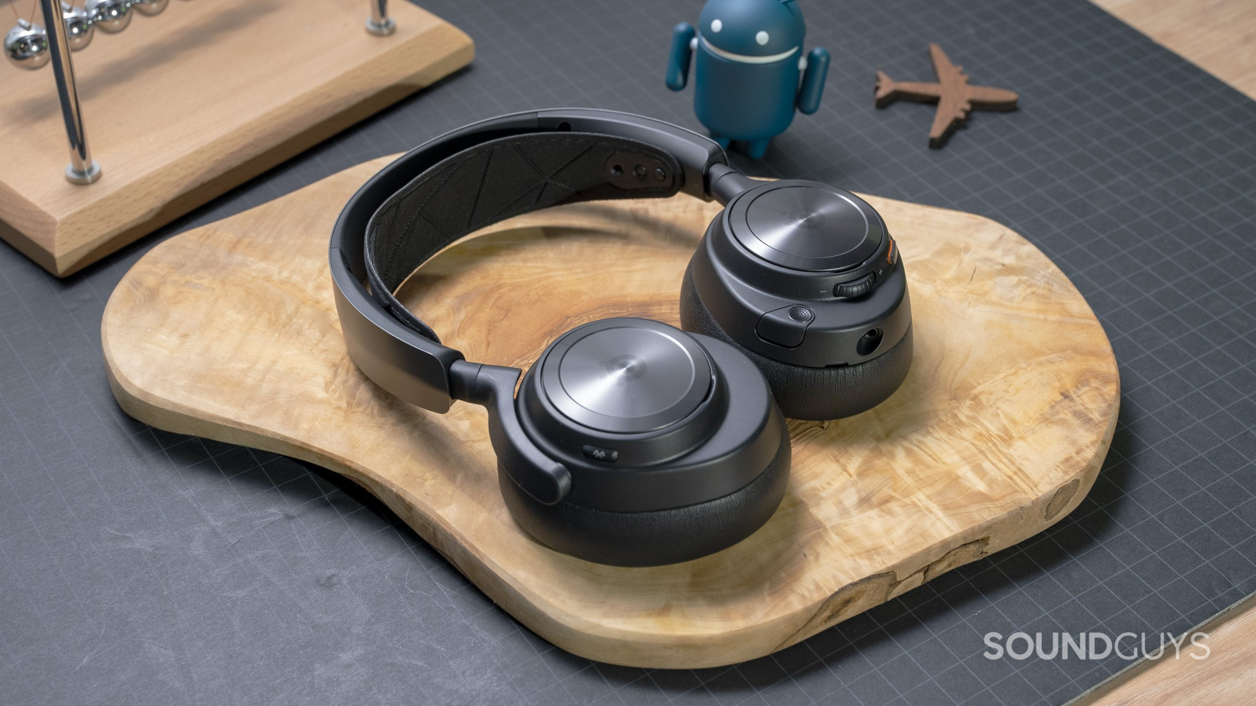 SteelSeries Arctis Nova Pro Wireless flat beauty shot 2 The SteelSeries Arctis Nova Pro Wireless laid flat on a wooden board atop a grey surface.