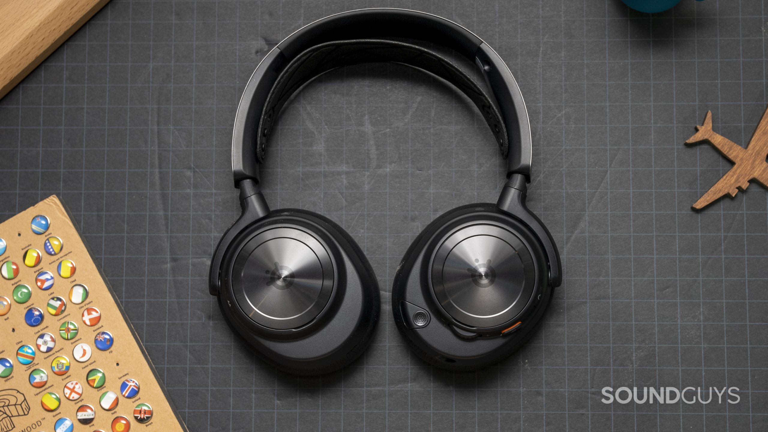 SteelSeries Arctis Nova Pro Wireless flat beauty shot The SteelSeries Arctis Nova Pro Wireless laid flat on a grey surface next to a wooden board.