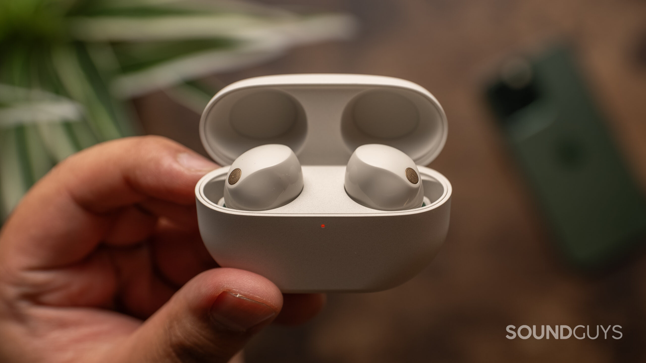 Holding Sony WF-1000XM5 charging case with earbuds inside One hand holding the Sony WF-1000XM5 inside of the charging case with the lid open