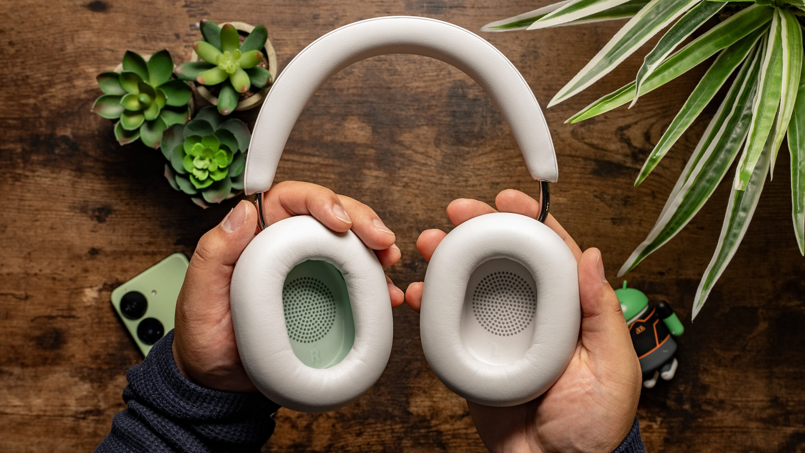 Sonos Ace in hand ear cups facing camera Top down photo of a man holding the Sonos Ace with the ear cups facing outwards to the camera with wooden board background