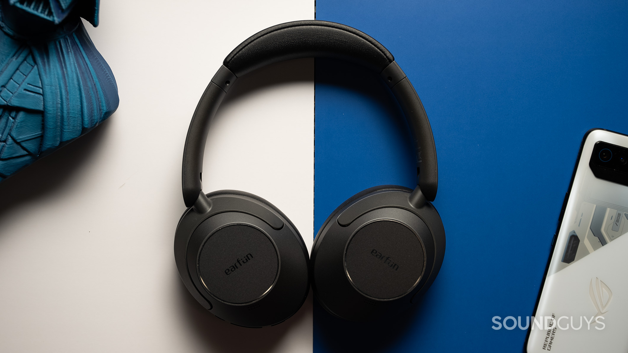 EarFun Wave Pro next to phone 2 EarFun Wave Pro on blue and white background next to phone and figurine.
