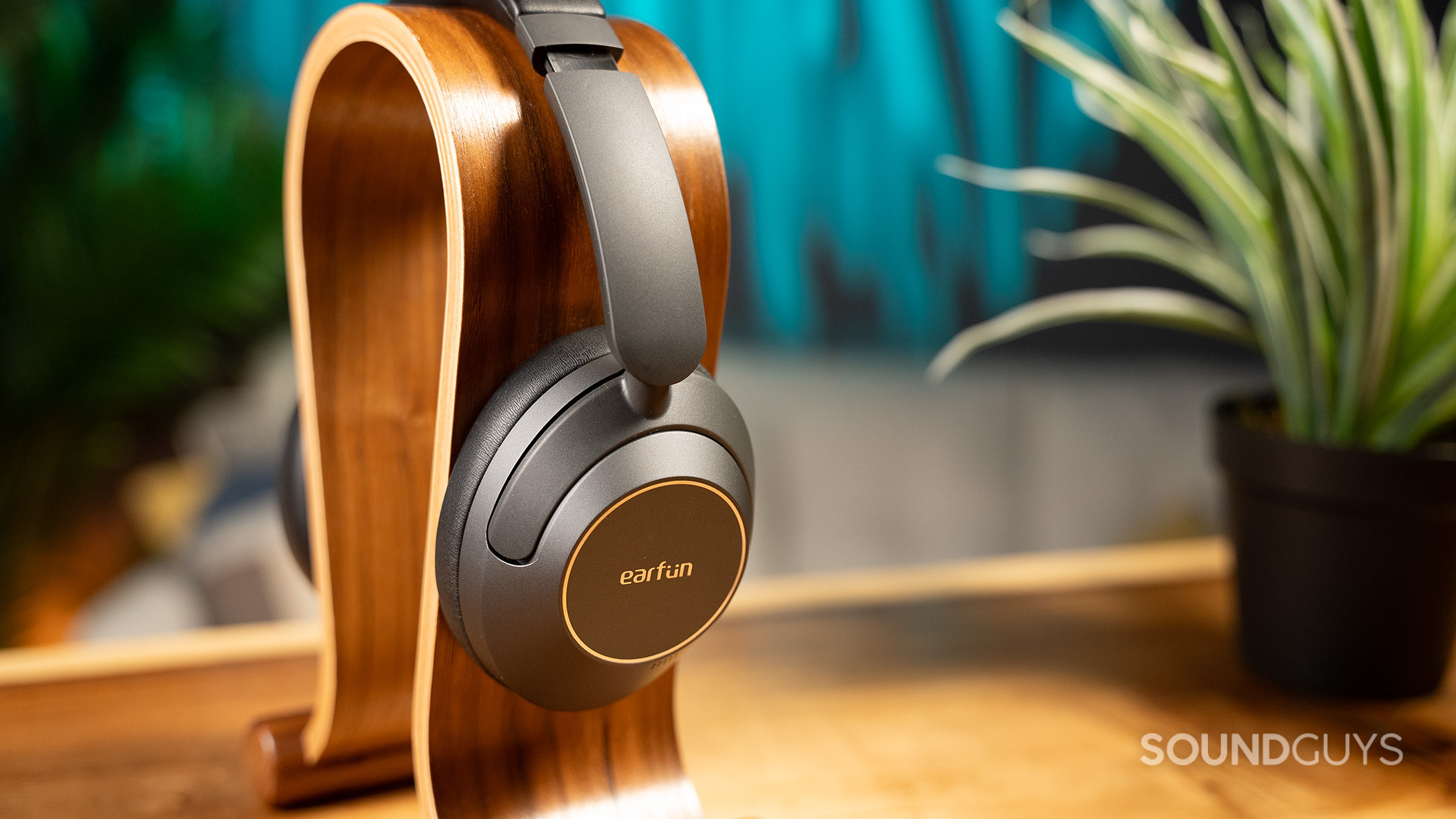 EarFun Wave Pro on headphone stand EarFun Wave Pro headphones on a wood stand next to a plant.