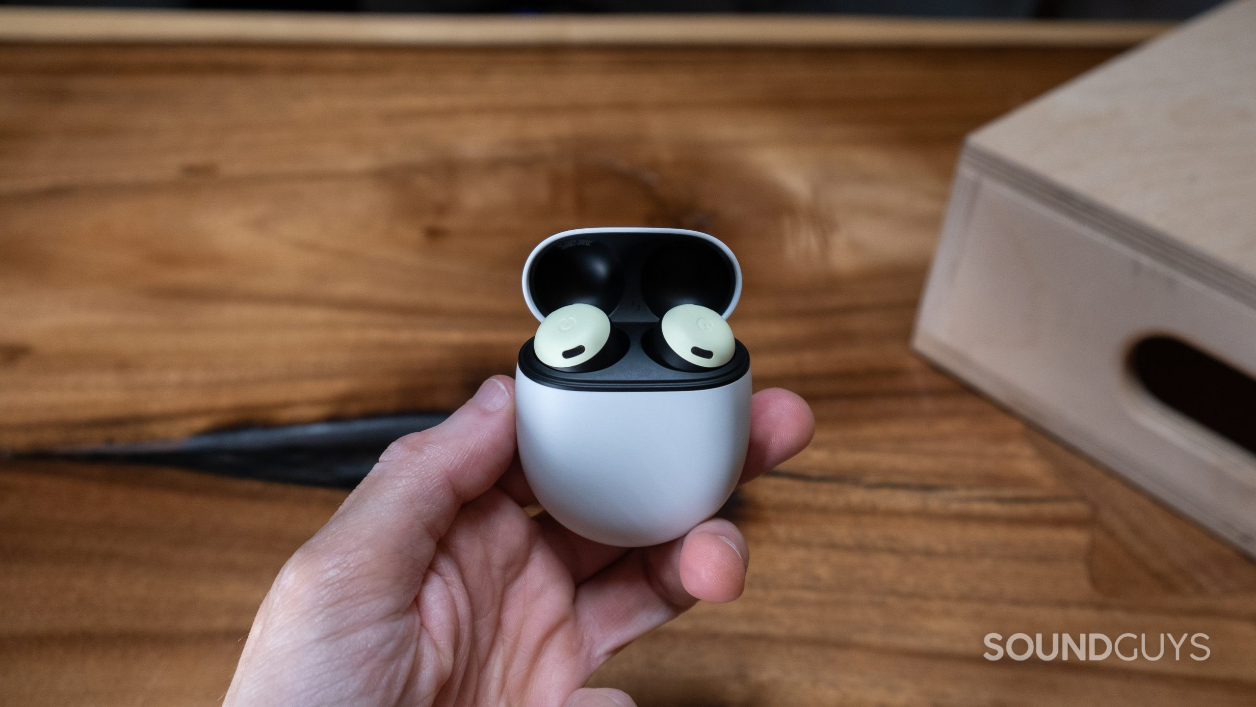google-pixel-buds-open-center.in-hand A hand holds the Google Pixel Buds Pro with the case open in front of a wood surface.
