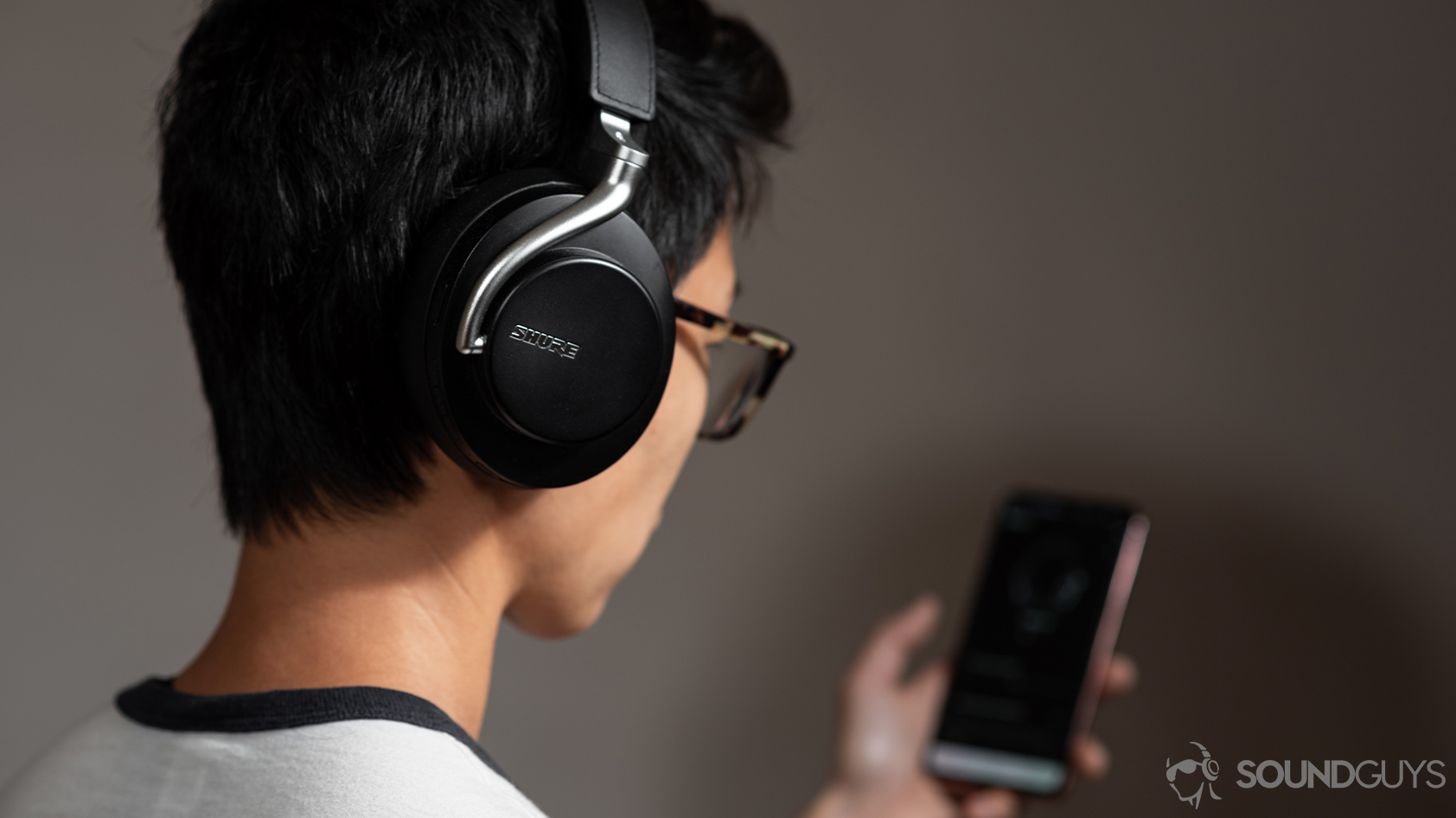 headphone data collection-Shure AONIC 50 PlayPlus app A woman wearing the Shure AONIC 50 noise canceling headphones and using the Shure PlayPlus headphone app.