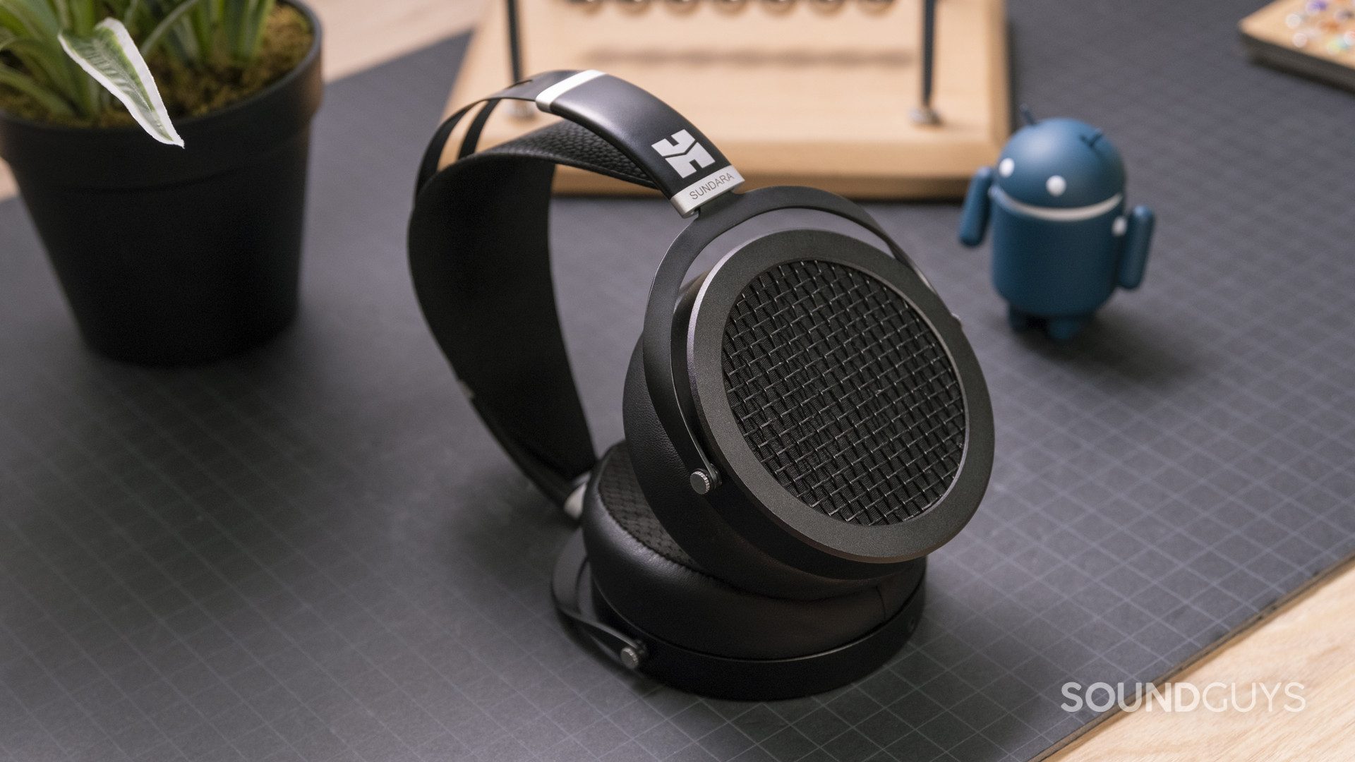 hifiman-sundara-hero The HiFiMan Sundara open-back planar headphones in full view on a gridded surface with wooden accessories in the background.