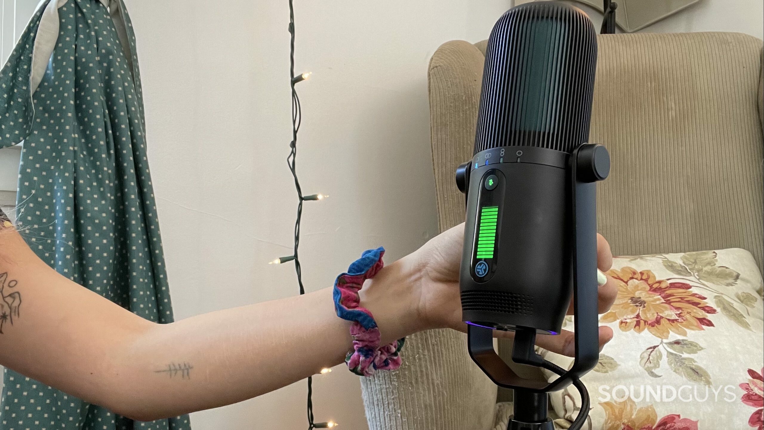 JLab Talk PRO USB microphone hand A womans hand using the JLab Talk PRO USB microphone with an armchair in the background.