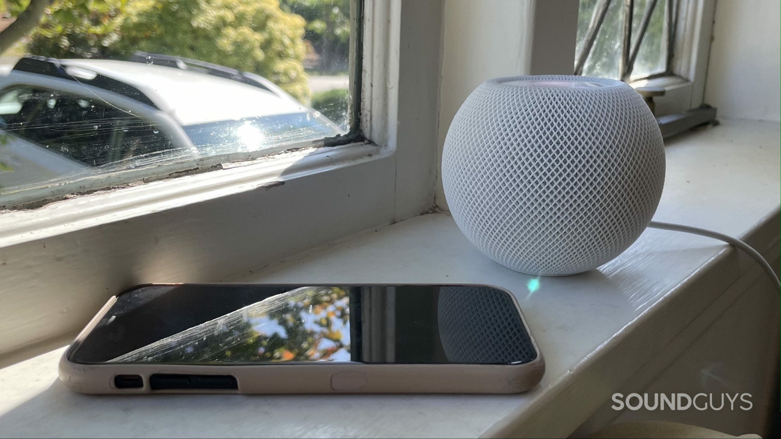 Apple Homepod mini iPhone window An iPhone and Apple HomePod mini on a windowsill.