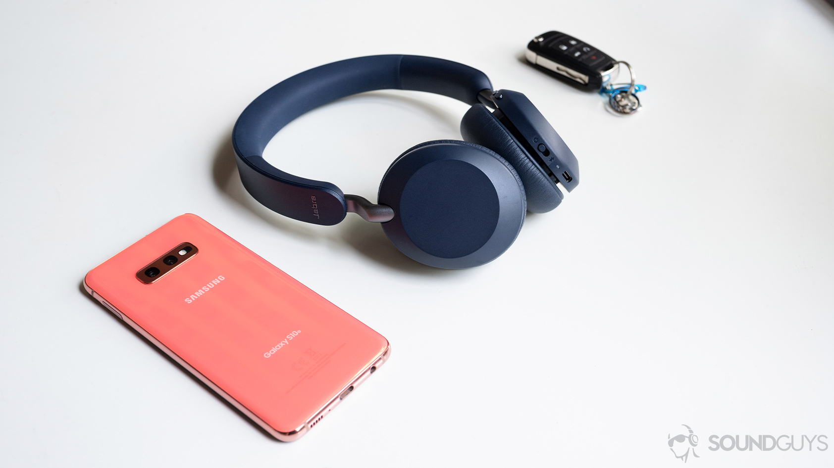 Jabra Elite 45h-wireless on ear headphones Samsung smartphone The Jabra Elite 45h on-ear Bluetooth headphones next to a Samsung Galaxy S10e smartphone and wireless car keys on a white table.