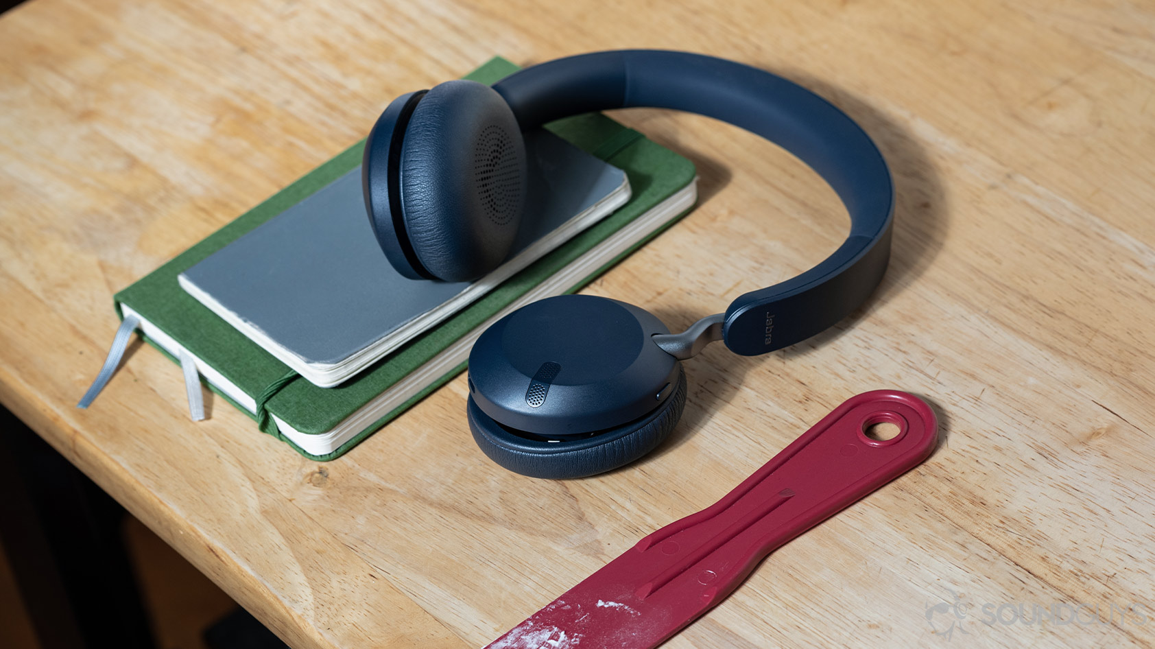 Jabra Elite 45h-wireless on ear headphones table books The Jabra Elite 45h on-ear Bluetooth headphones on a wooden surface with journals; the left ear cup is rotated so the interior padding is visible to the viewer.