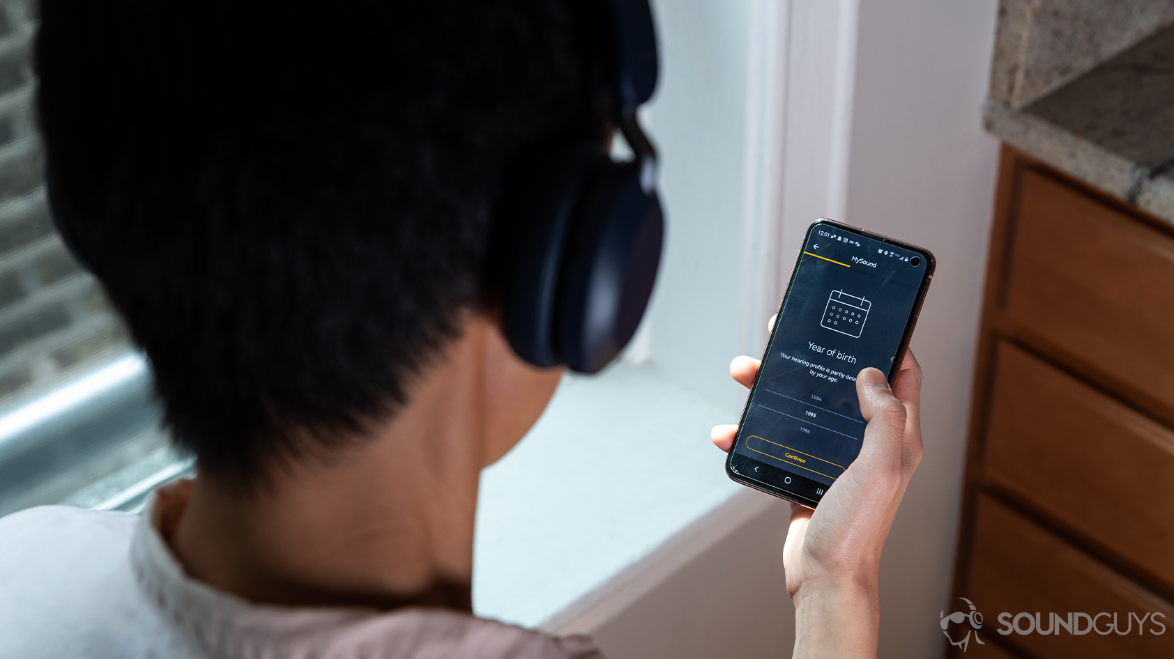 Jabra Elite 45h-wireless on ear headphones woman wearing MySound app An over-the-shoulder picture of the Jabra Elite 45h on-ear Bluetooth headphones connected to the Jabra MySound+ application on a smartphone held by a woman.