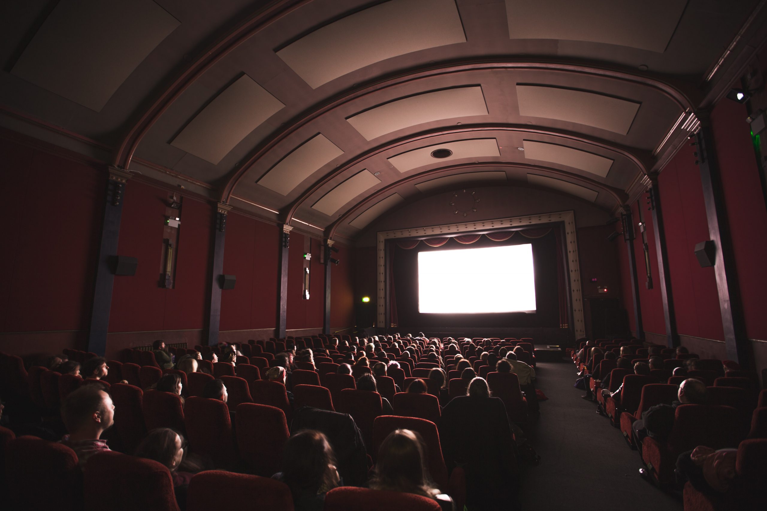 jake-hills-23LET4Hxj_U-unsplash People watching a movie screen seen from back of the theater