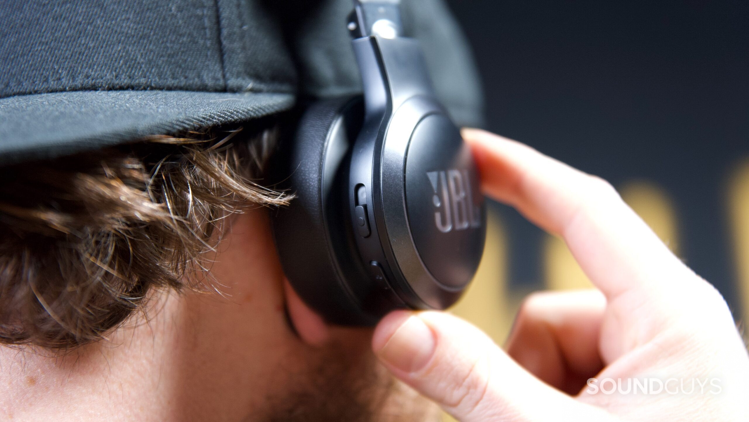 JBL Love 670NC controls A man pressing the control buttons on a pair of JBL Live 670NC headphones