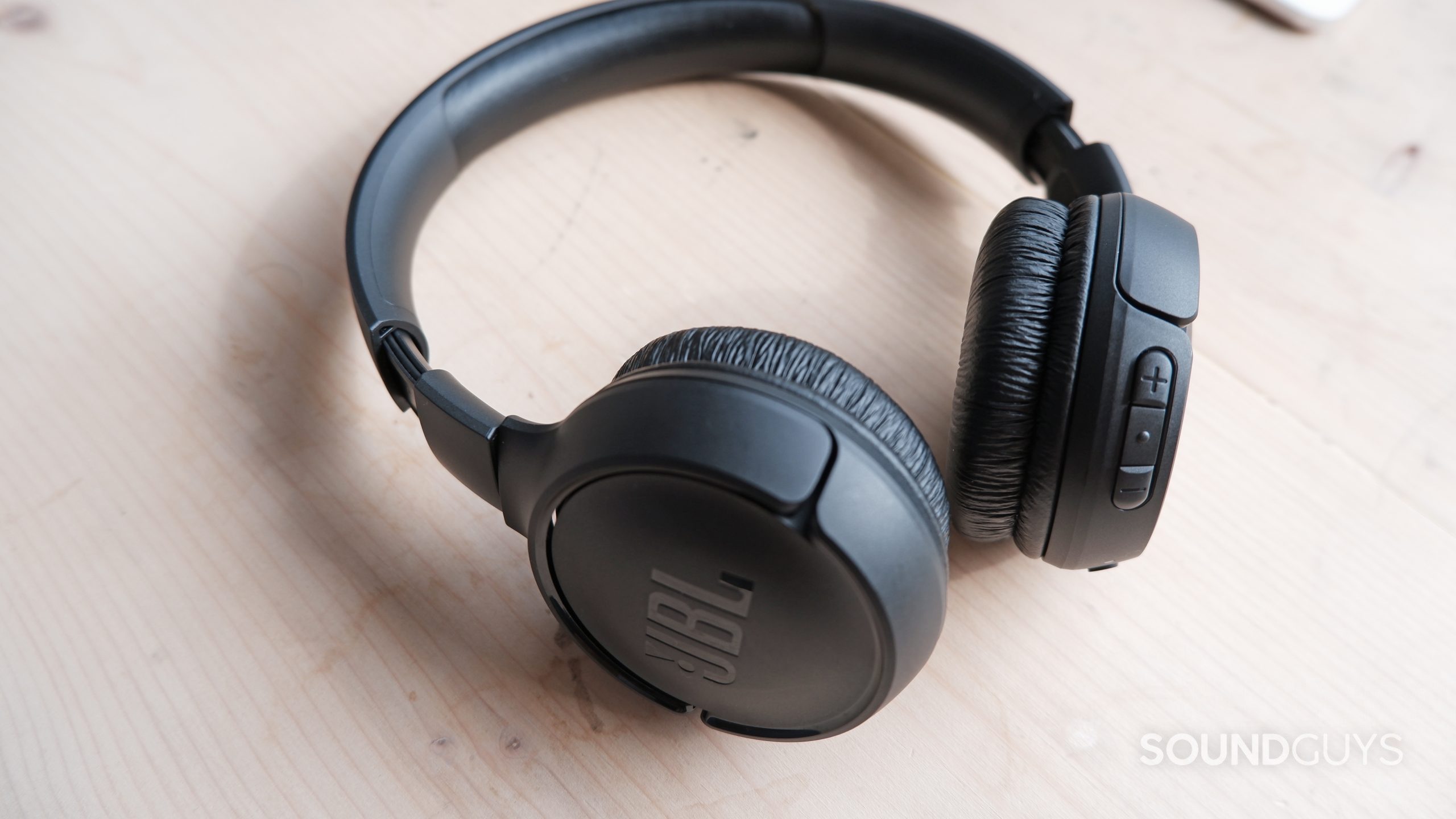 JBL-tune-510bt-wood-table The JBL Tune 510BT headset on a wooden table, showing the volume buttons and ear cups.