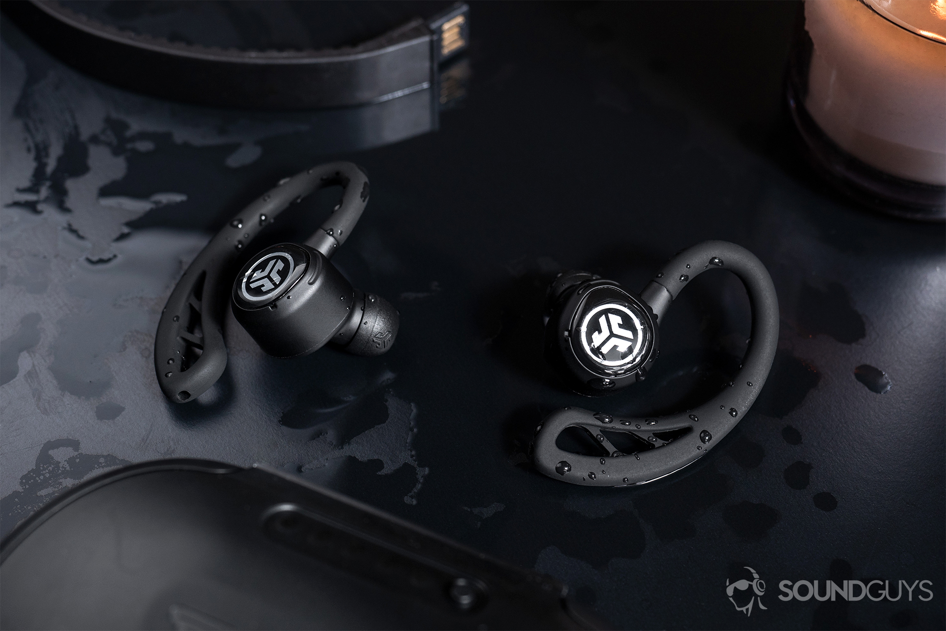 JLab_Epic Air Elite-6 The earbuds surrounded by water on a black table.