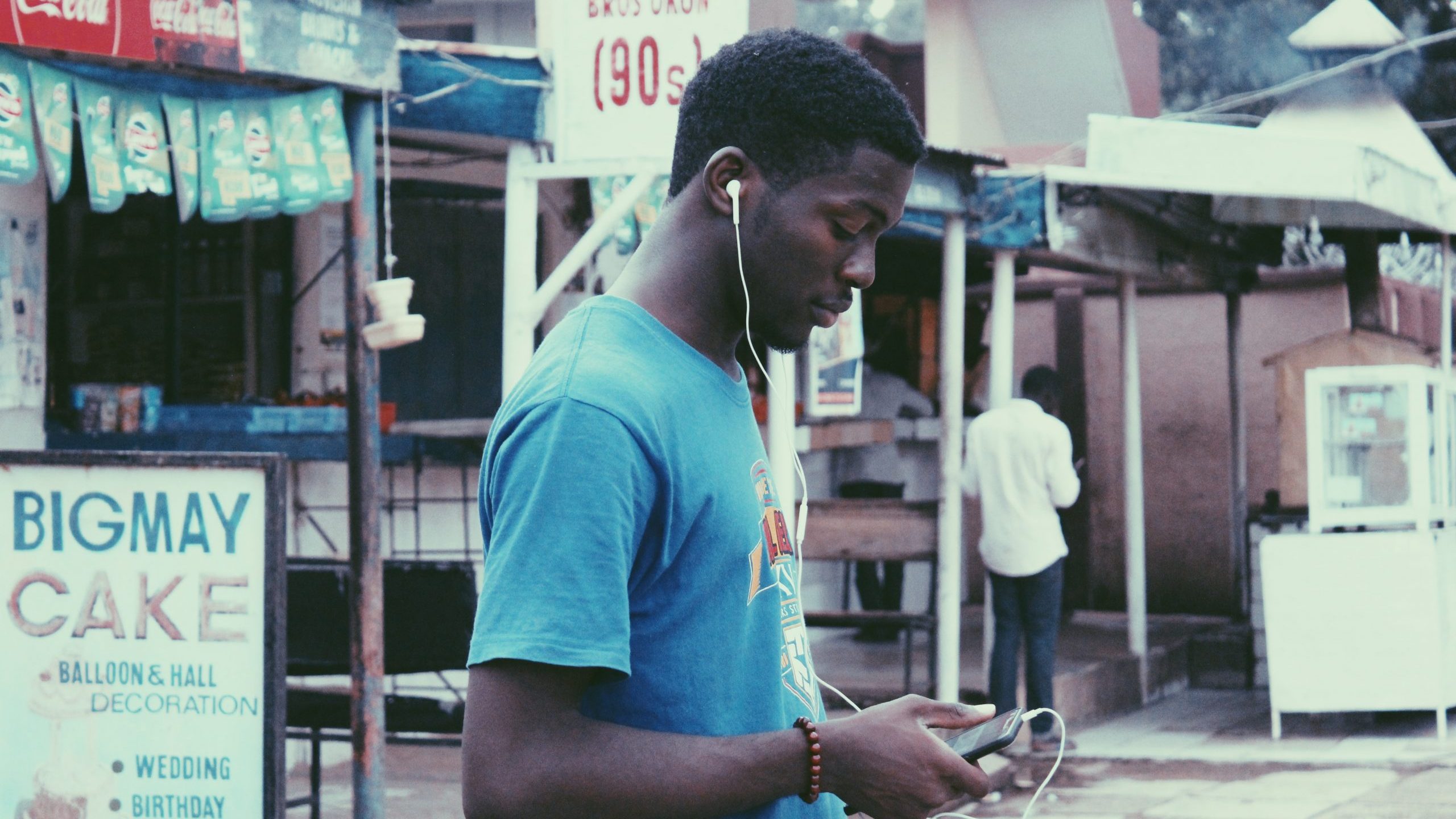 muhammadtaha-ibrahim-ma-aji-z9mq3SP9uy4-unsplash Man on the street using wired earbuds with a cellphone