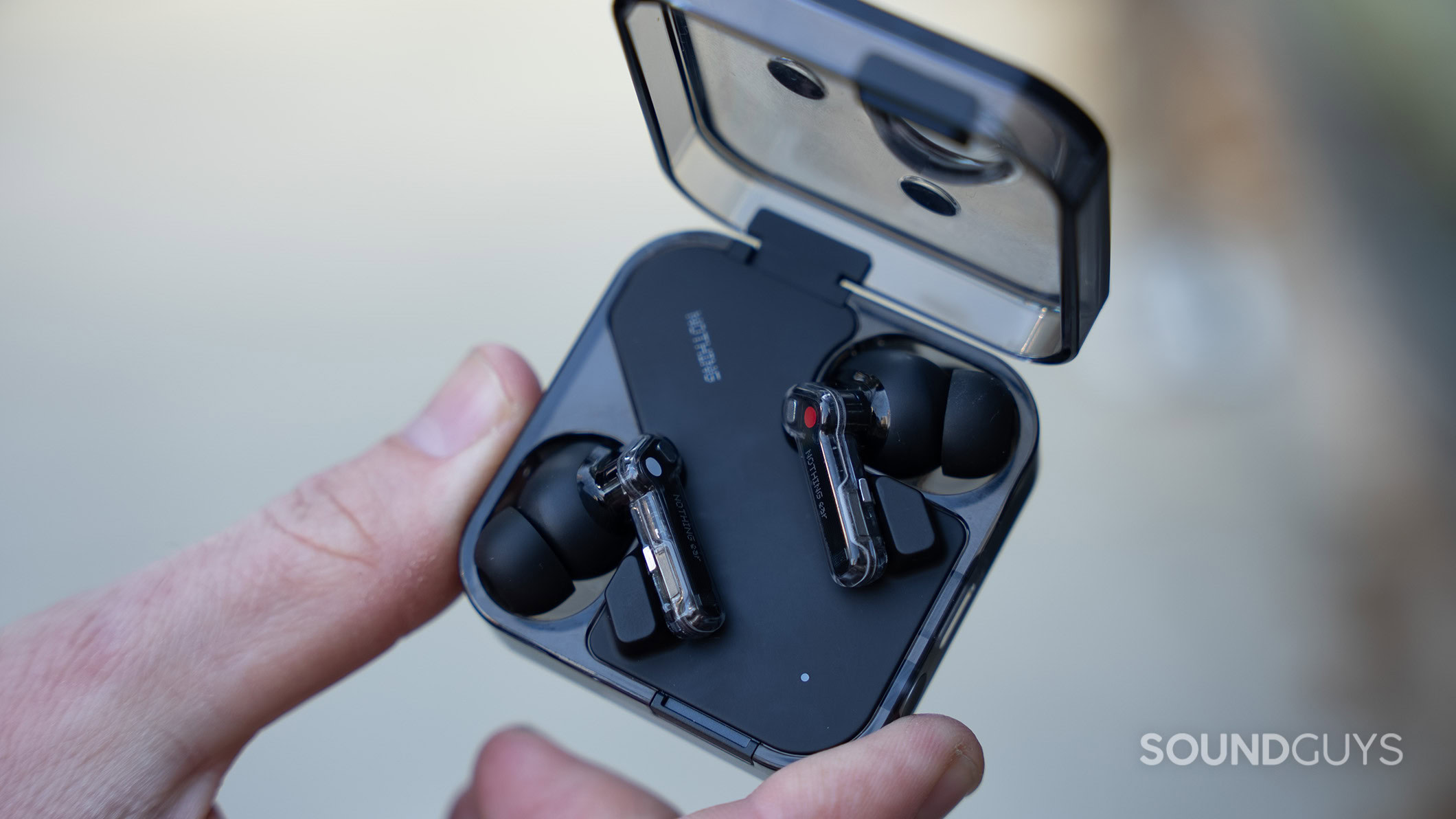 Nothing Ear earbuds in case in hand 2 Nothing Ear earbuds and charging case with the case lid open.