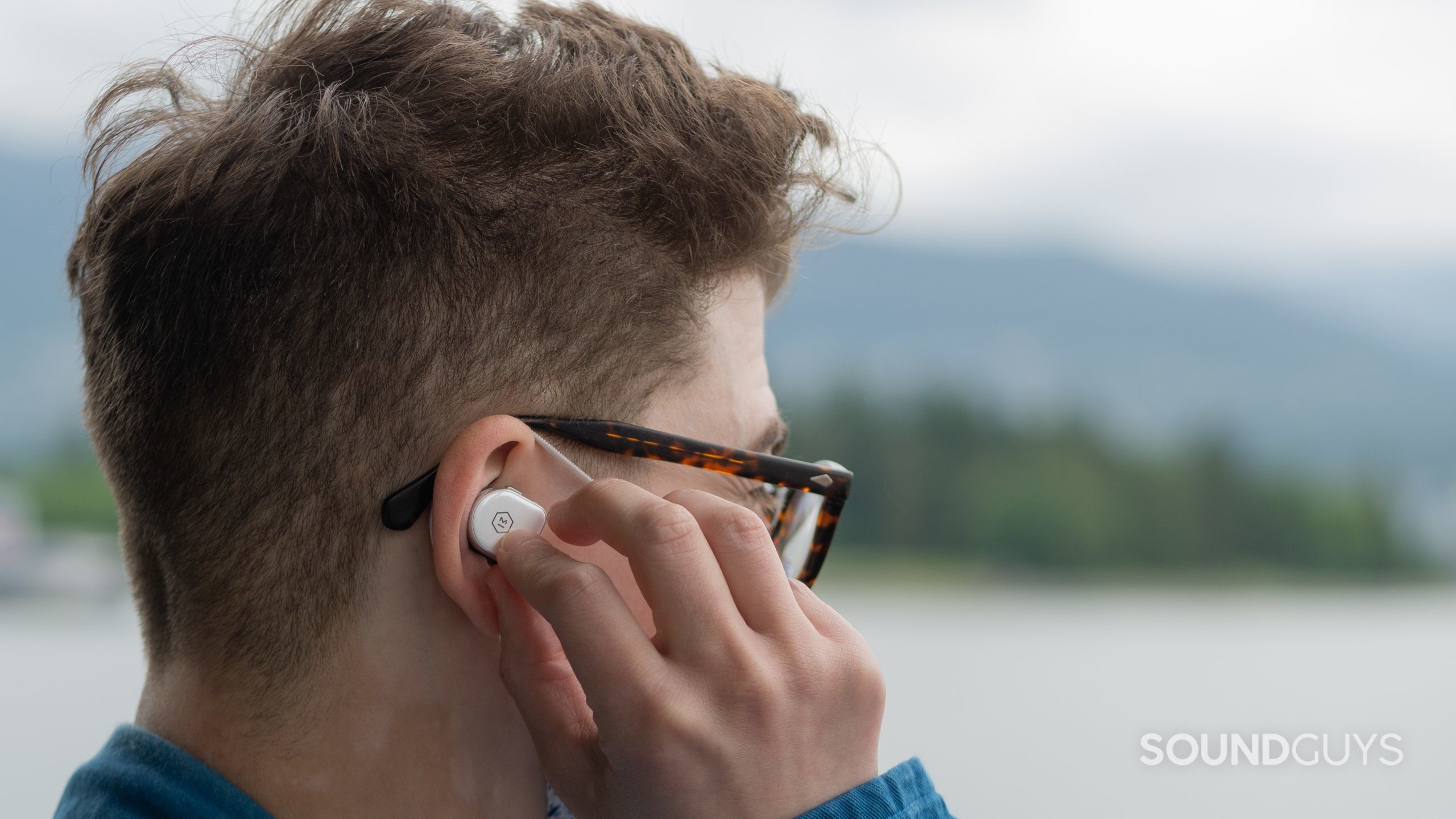 Master & Dynamic MW08 true wireless noise canceling earbuds man wears Here's a close up of a man holding master & dynamic MW08 earbud to his right ear.