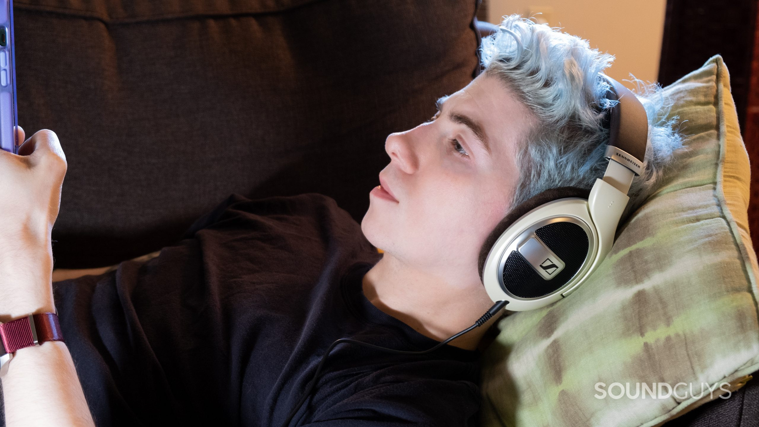 sennheiser-hd-599-on-ears A man on a couch rests his head on a pillow while wearing the Sennheiser HD 599 and looking at a phone.