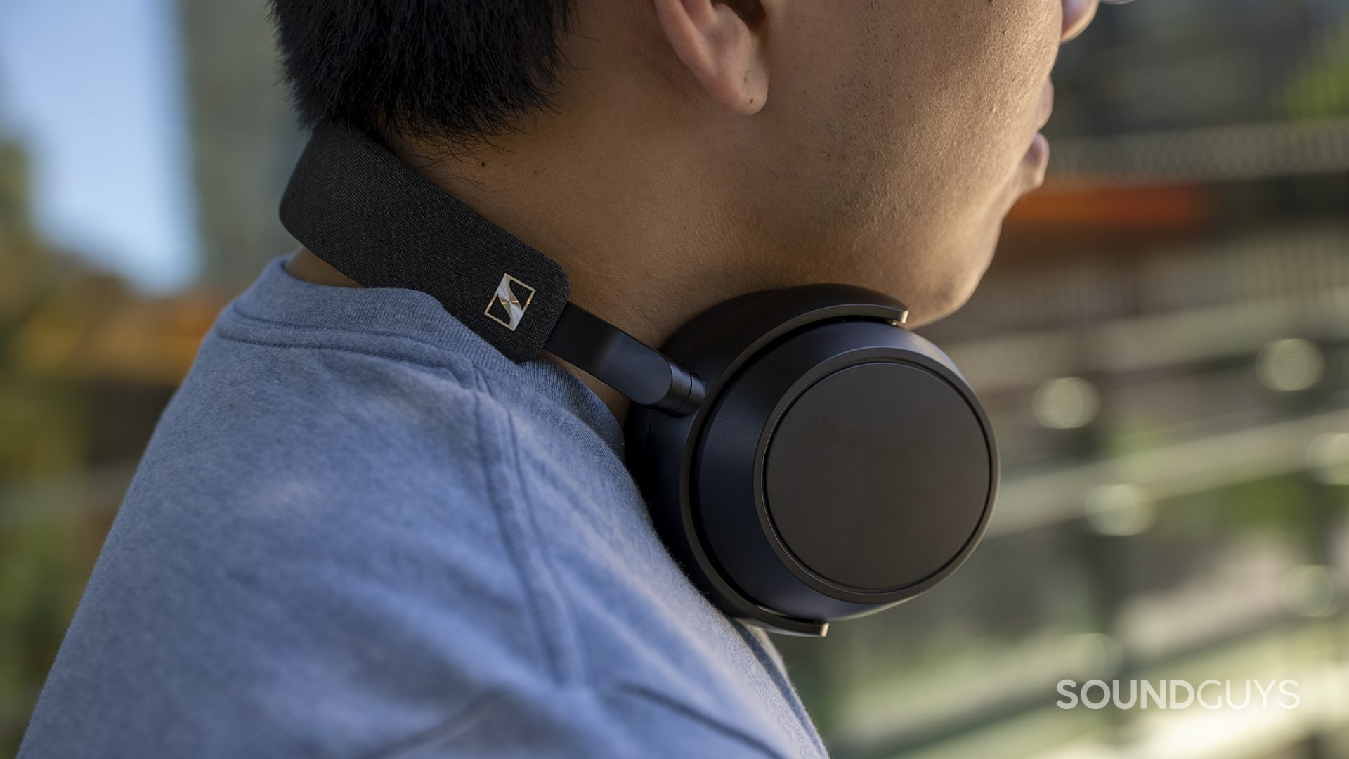 sennheiser-momentum-4-wireless-neck A man wears the Sennheiser MOMENTUM 4 Wireless around his neck while outside.