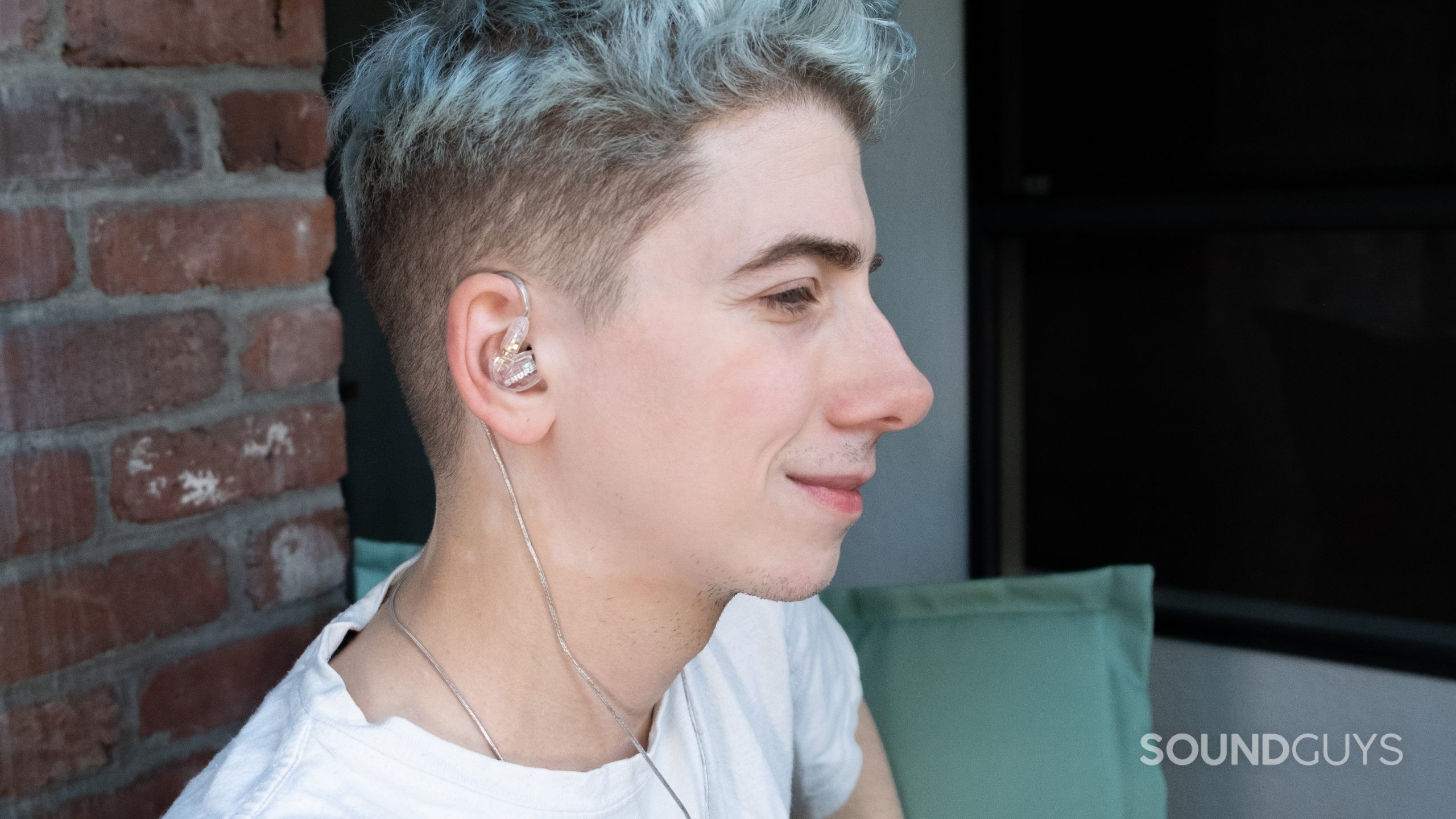 shure-se215-in-ears-outside A man faces right wearing the Shure SE215 cabled around the top of the ear with the cable running down behind the back of his ear.
